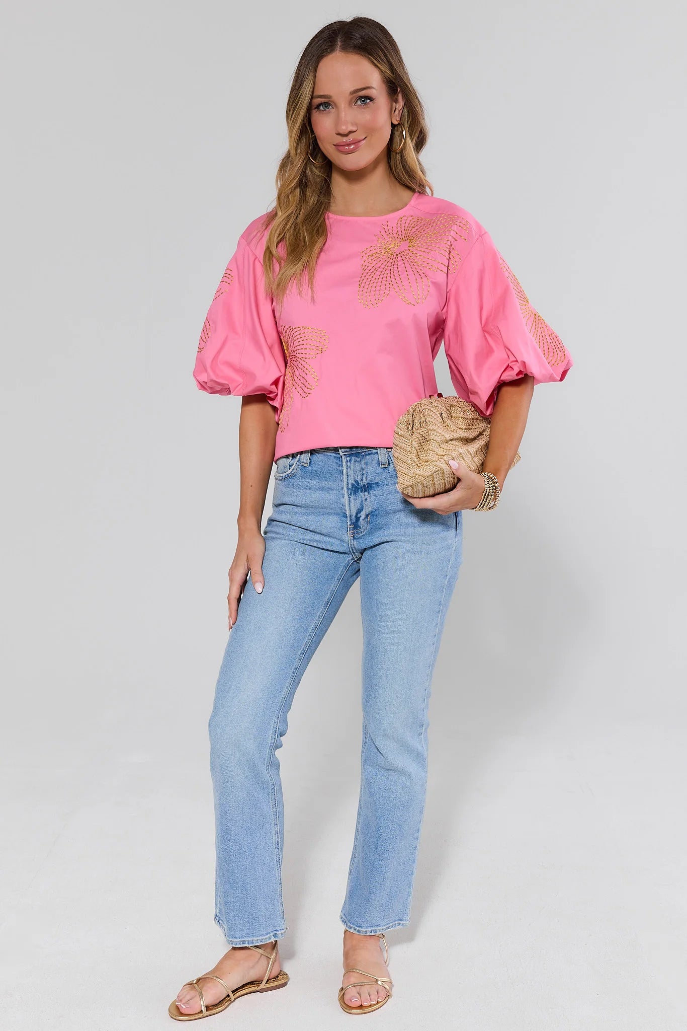 Woman wearing a pink tara blouse with floral design and blue jeans on a gray background