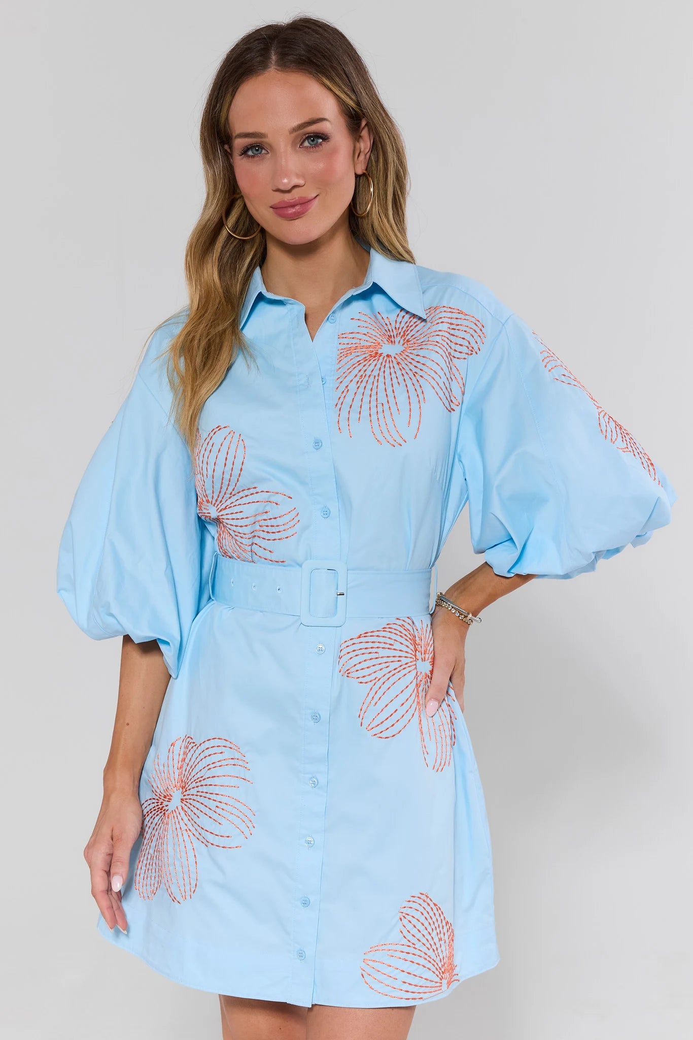 Woman wearing a light blue dress with floral patterns on a plain background