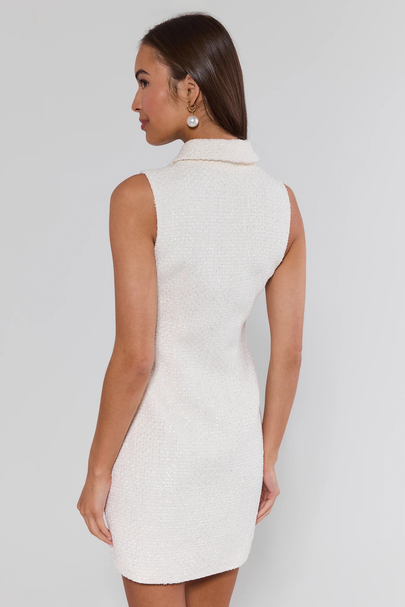 Woman wearing a white sleeveless dress against a plain background