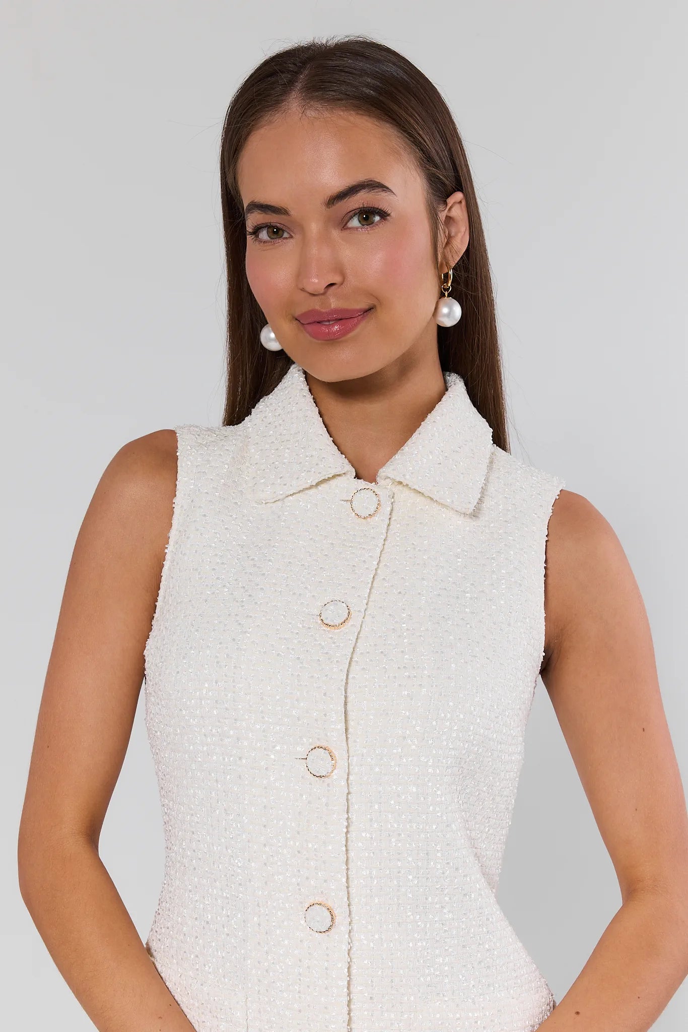 Woman wearing a white sleeveless button-up shirt against a plain background
