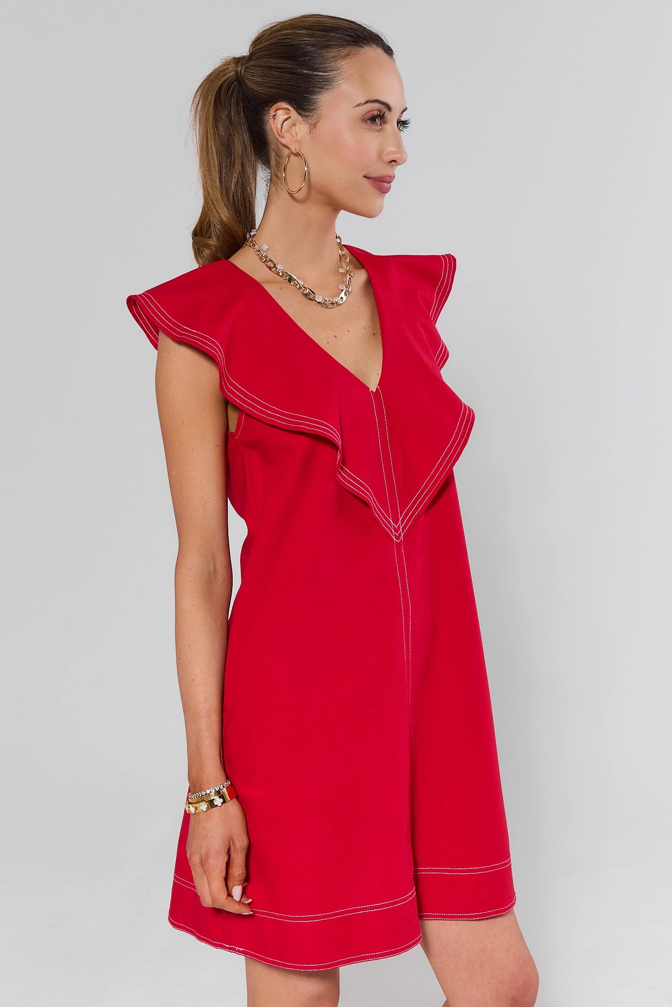 side shot Woman wearing a red dress with white trim on a gray background