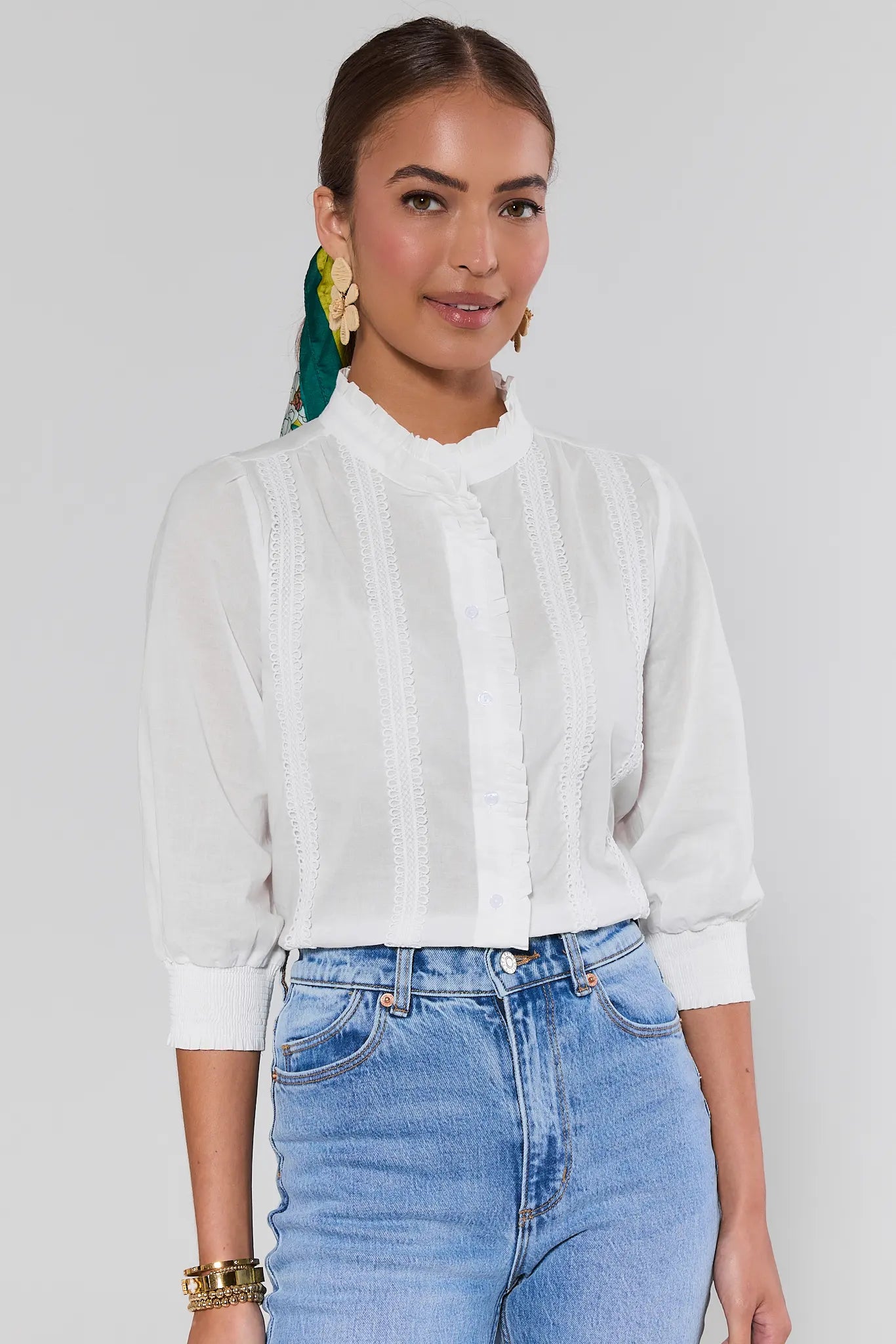 Woman wearing a white blouse and blue jeans against a plain background