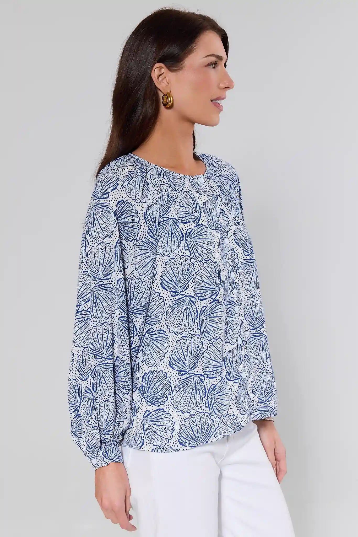 side shot Woman wearing a blue shell patterned blouse against a plain background