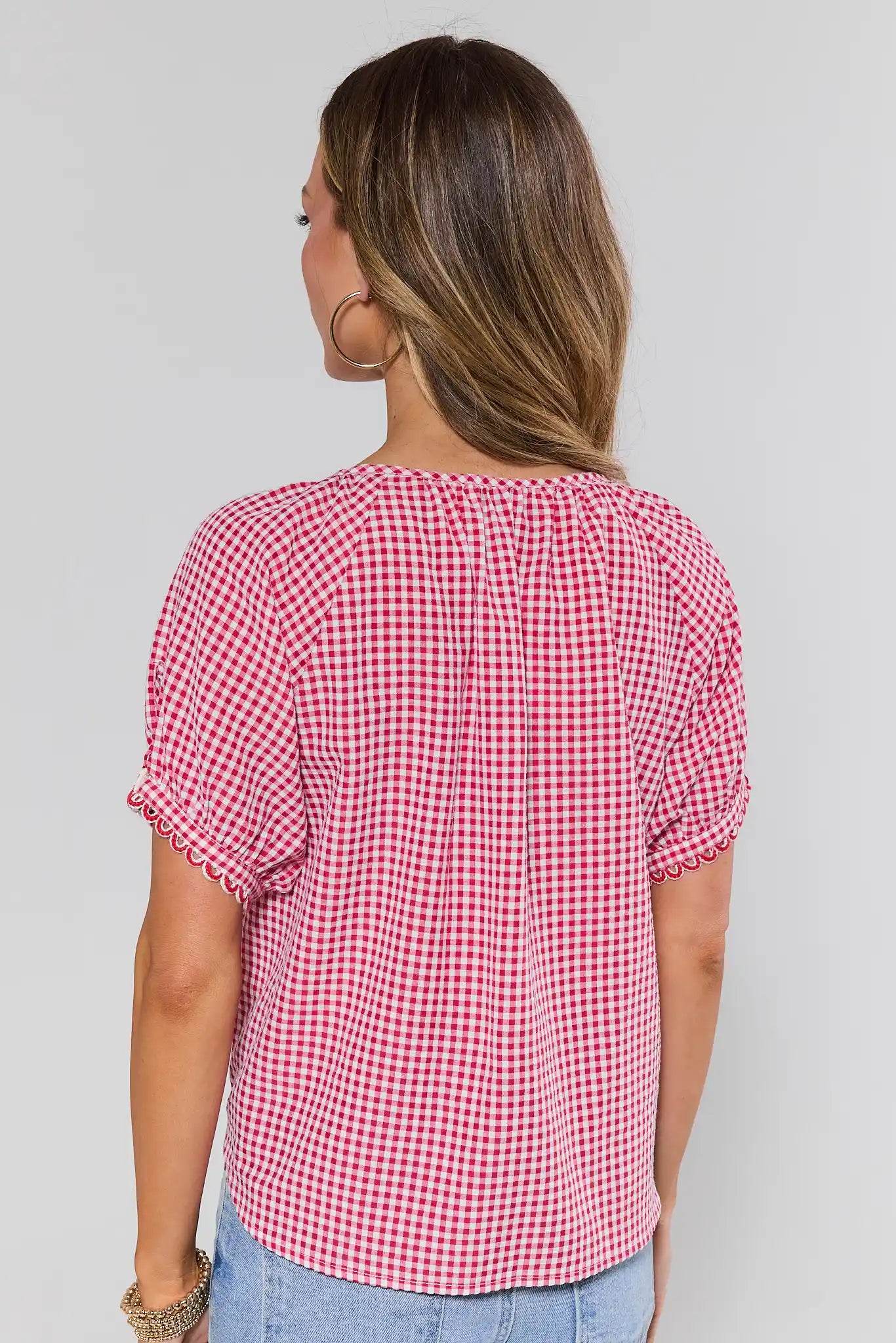 Woman standing wearing a red and white checkered blouse against a plain background