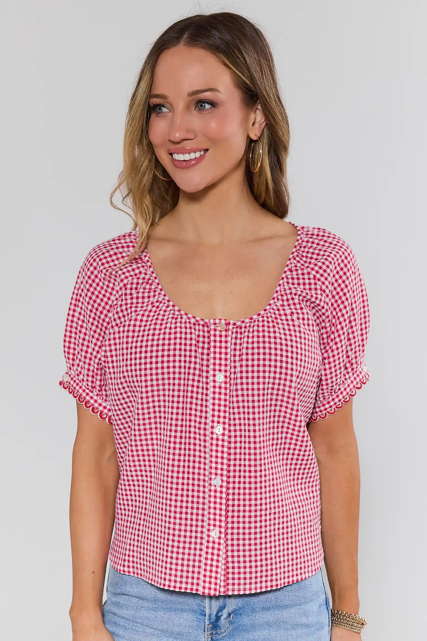 Woman wearing a red and white checkered blouse with short sleeves against a plain background