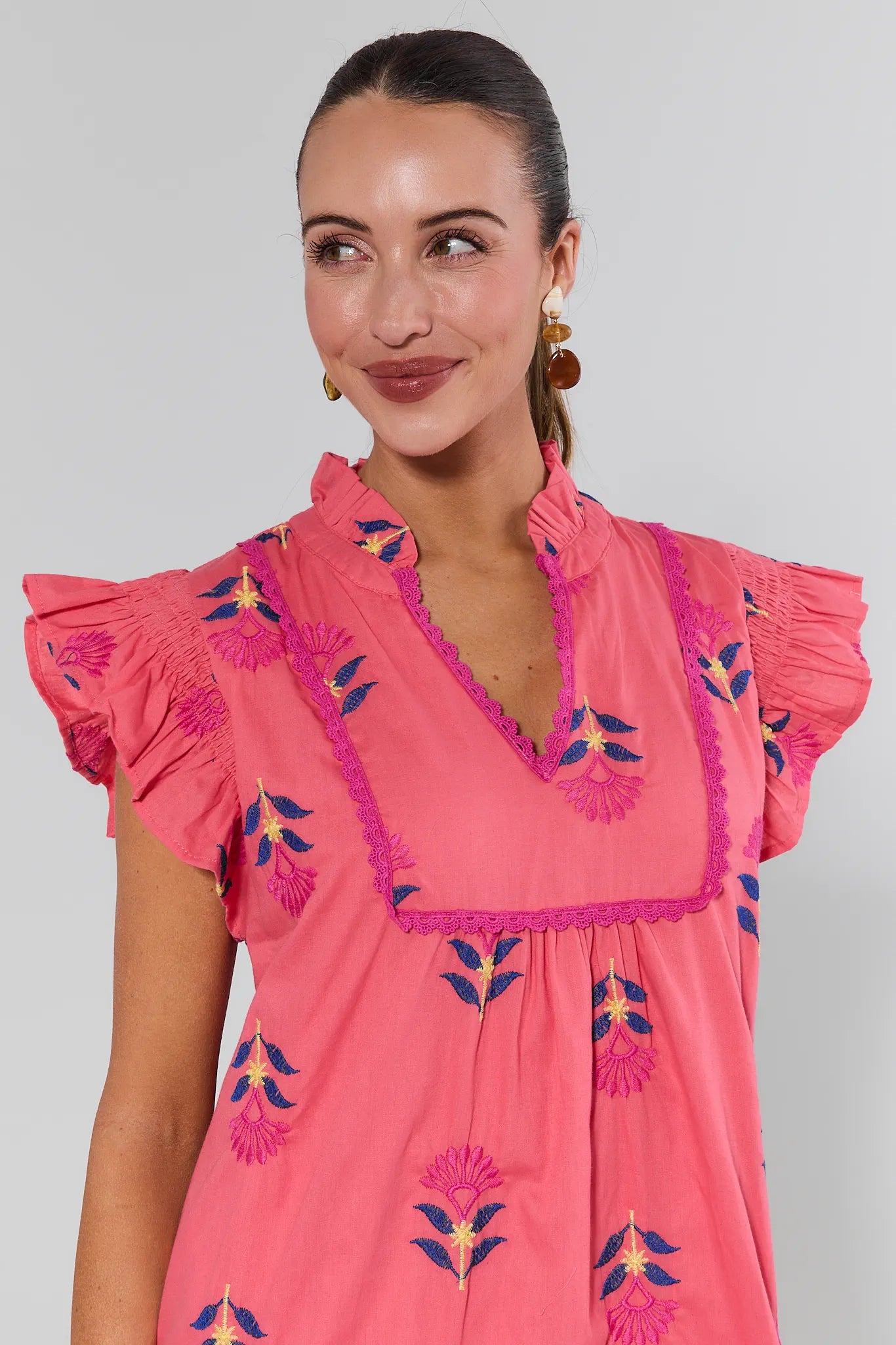 Woman wearing a pink embroidered dress against a plain background