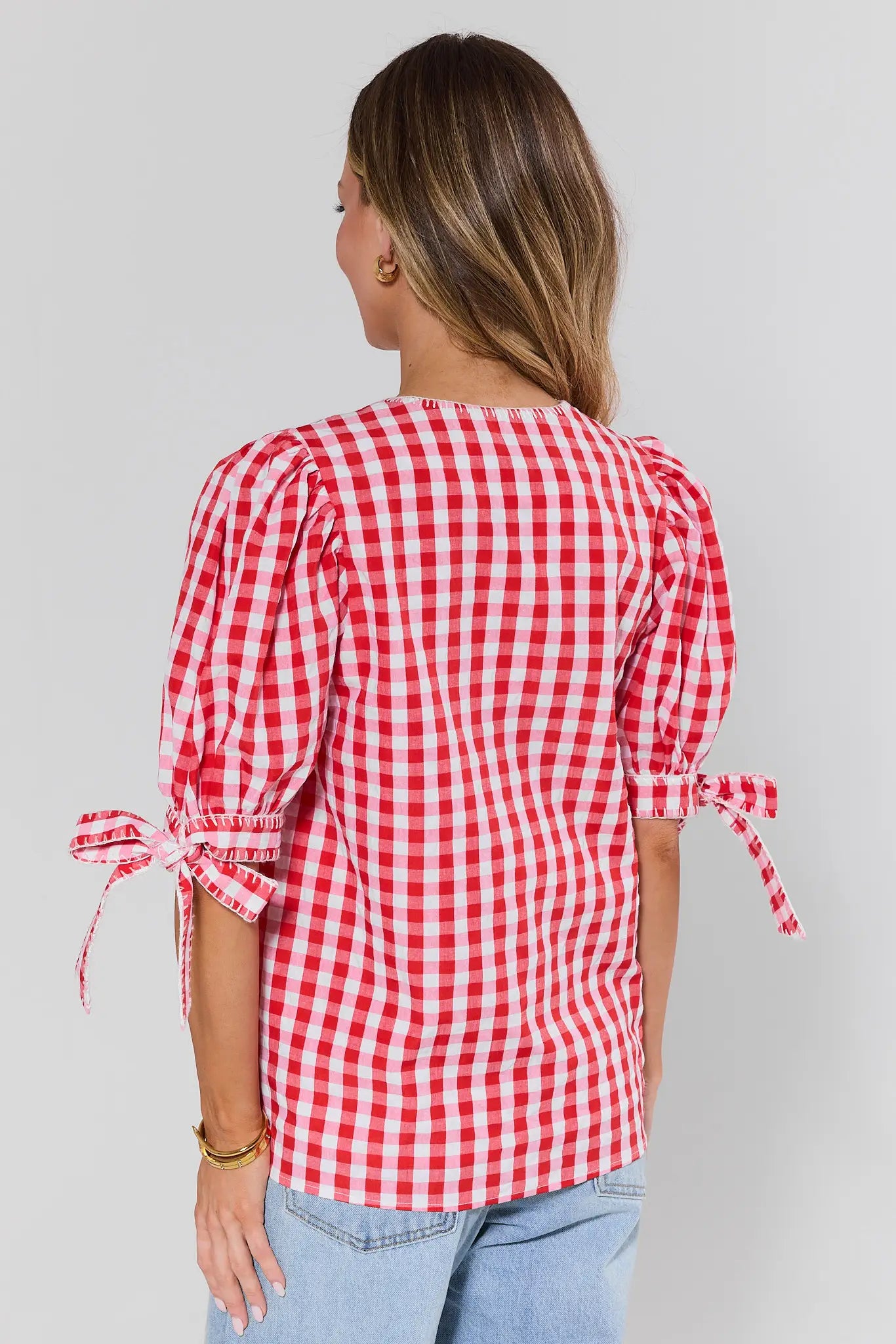 Woman standing wearing a red and white checkered blouse with tied sleeves on a gray background
