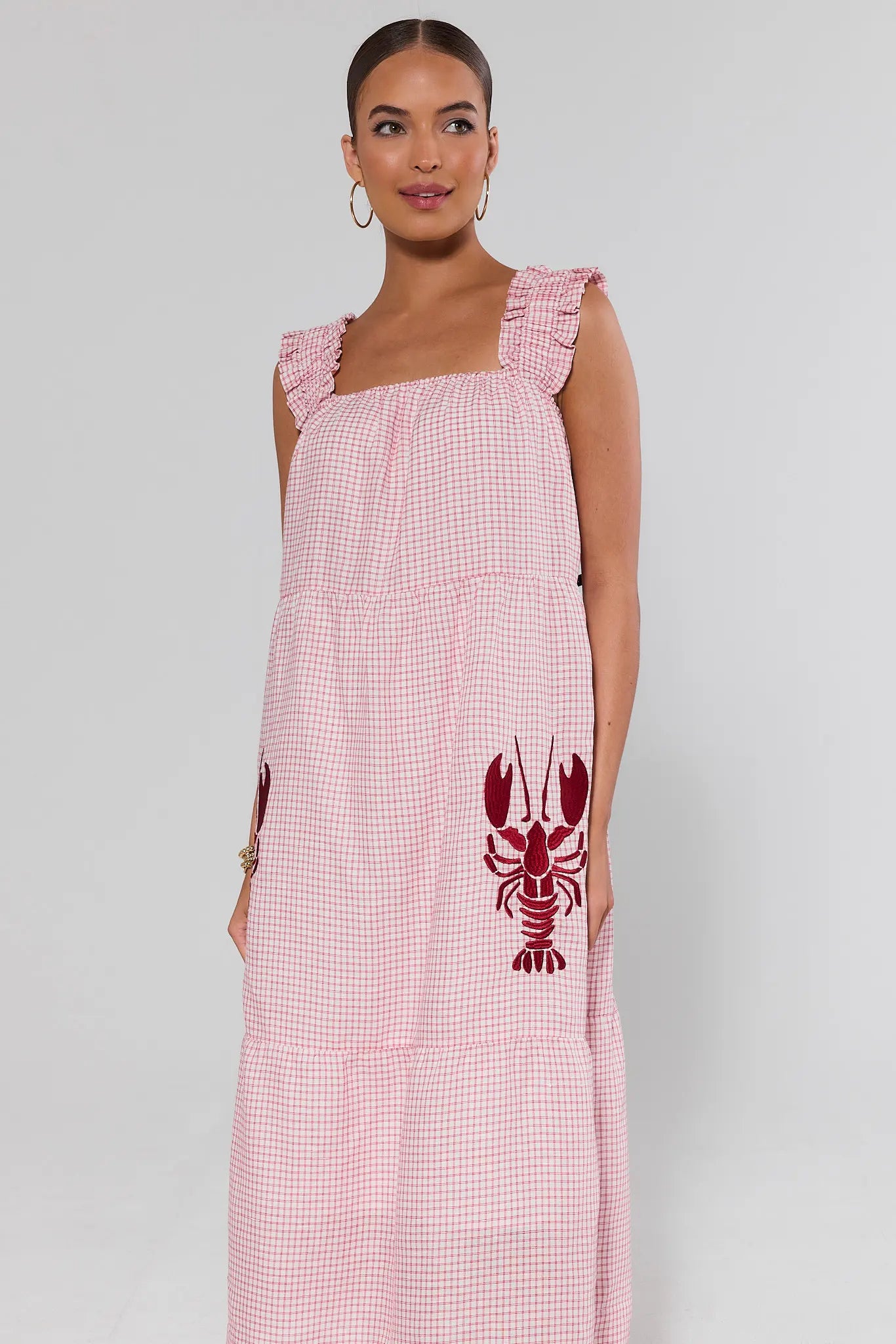 Woman wearing a pink gingham dress with a red lobster design on a white background