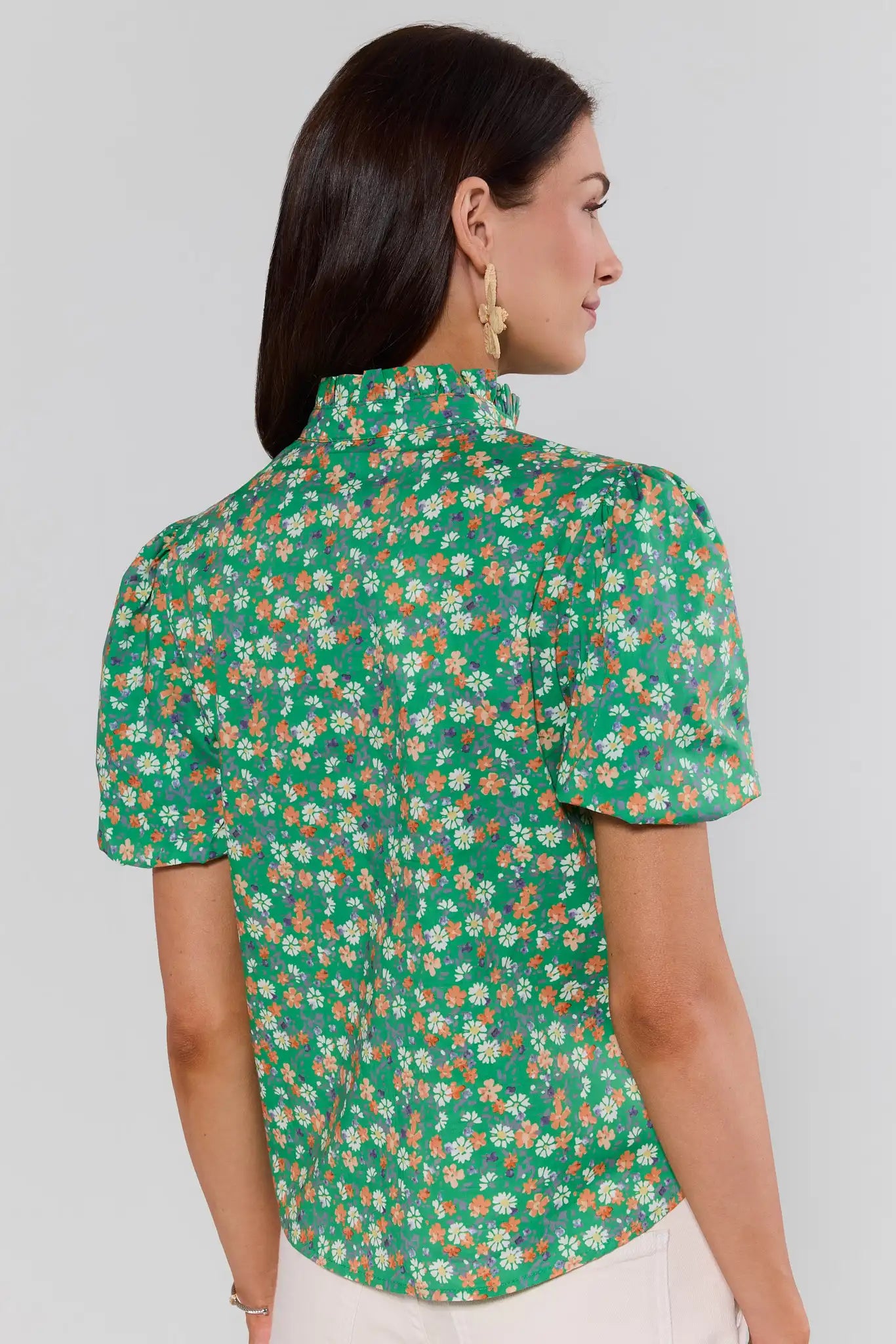Woman standing wearing a green floral blouse against a plain background