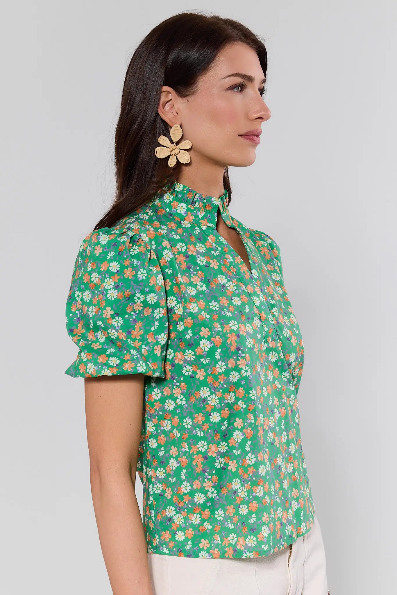 side shot Woman wearing a green floral blouse against a plain background