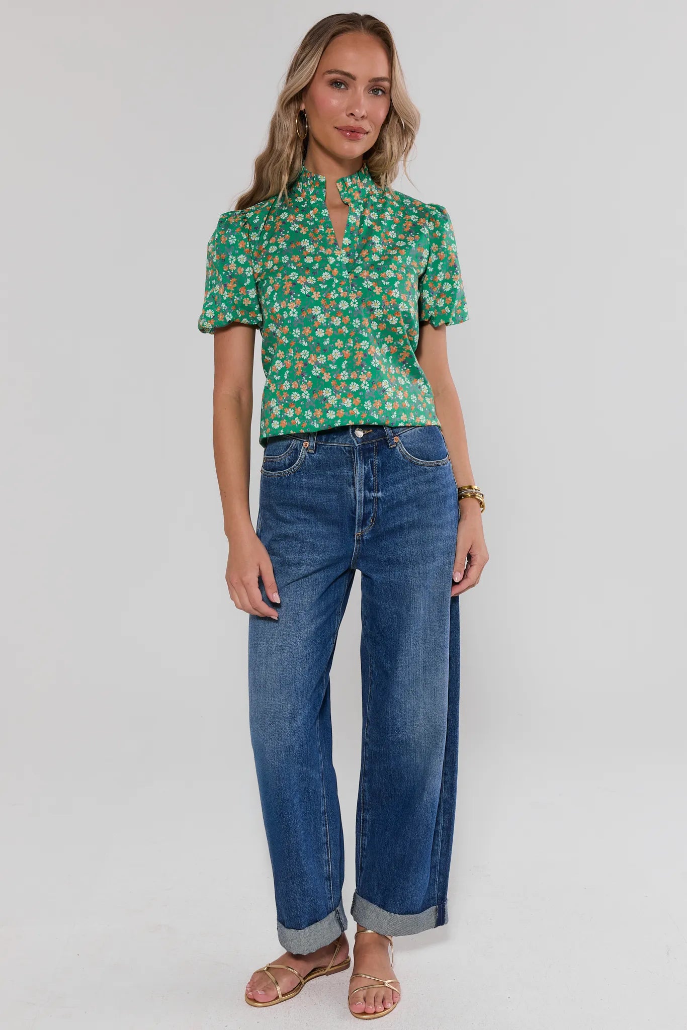 Woman wearing a green floral blouse and blue jeans on a white background