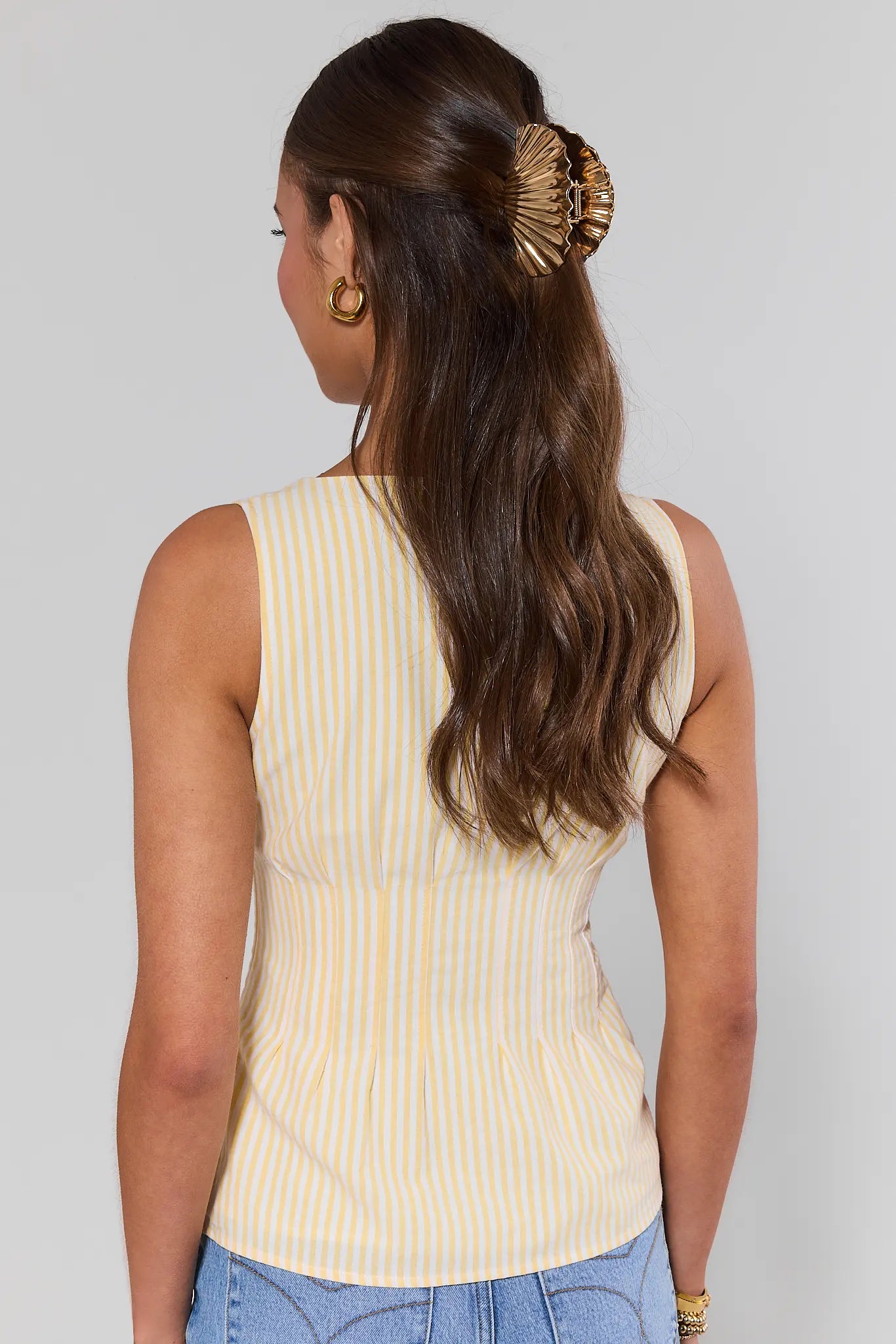 Woman standing wearing a yellow ribbed tank top with a plain background