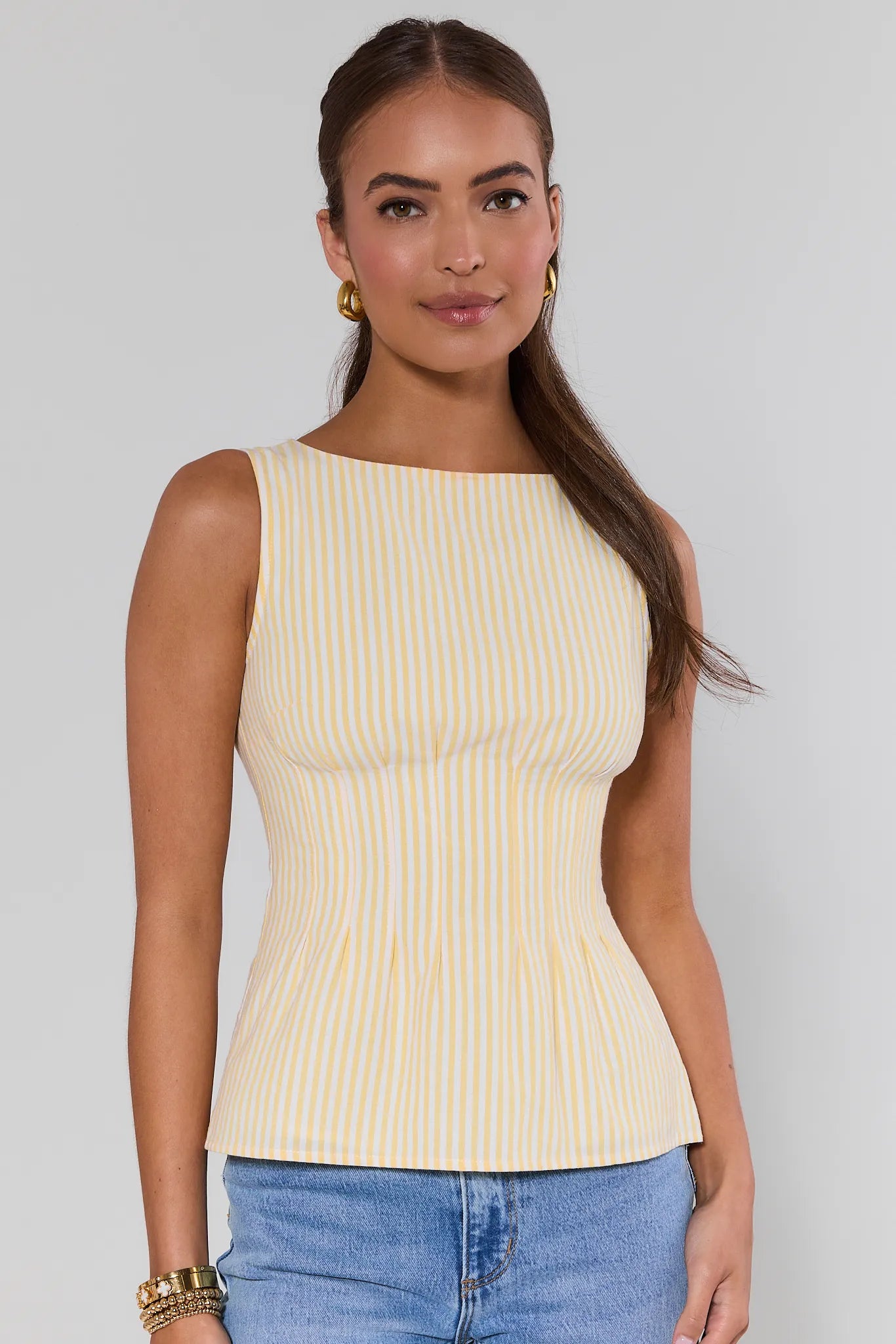 Woman wearing a yellow ribbed tank top and blue jeans against a gray background