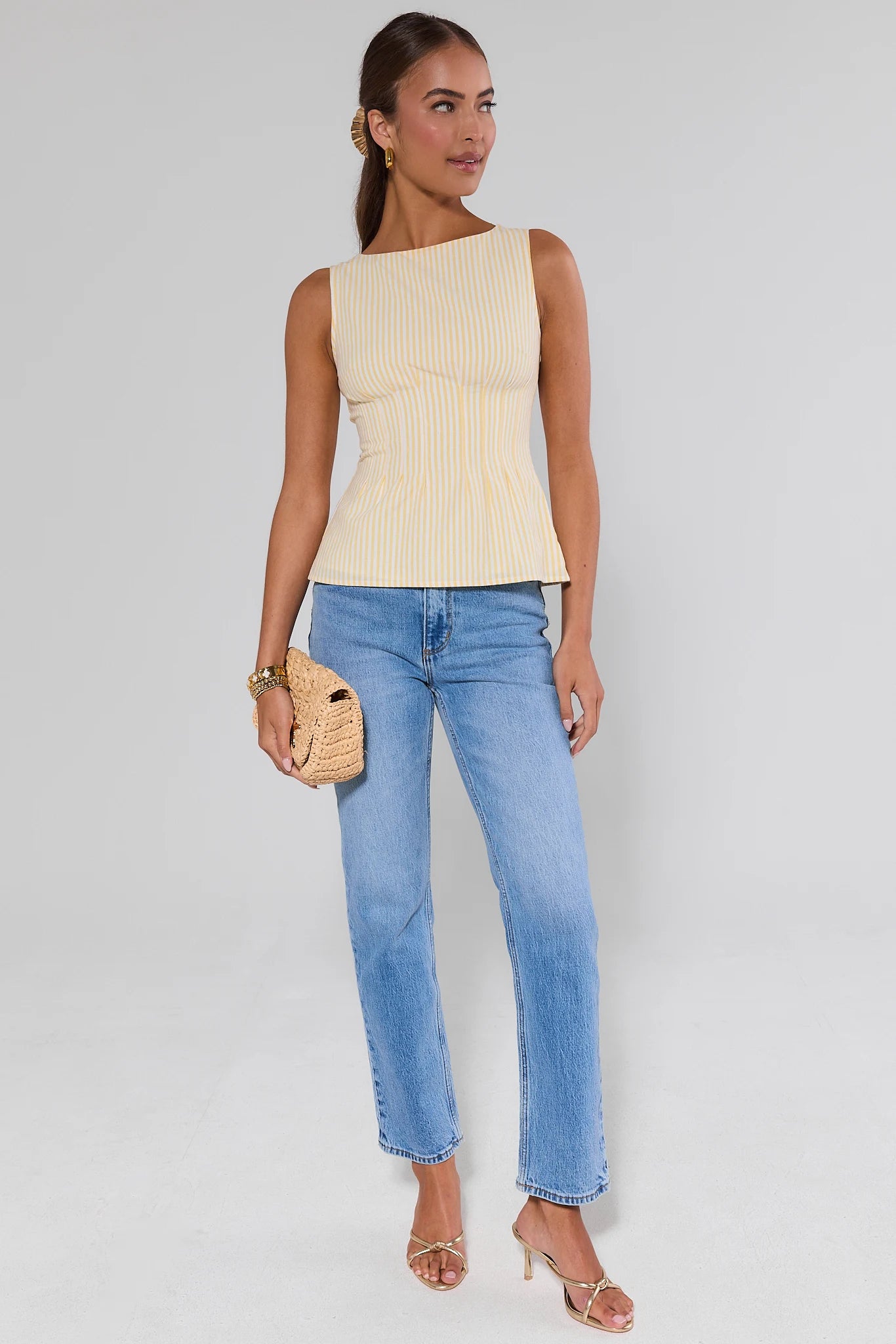 Woman wearing a cream sleeveless top and blue jeans against a white background