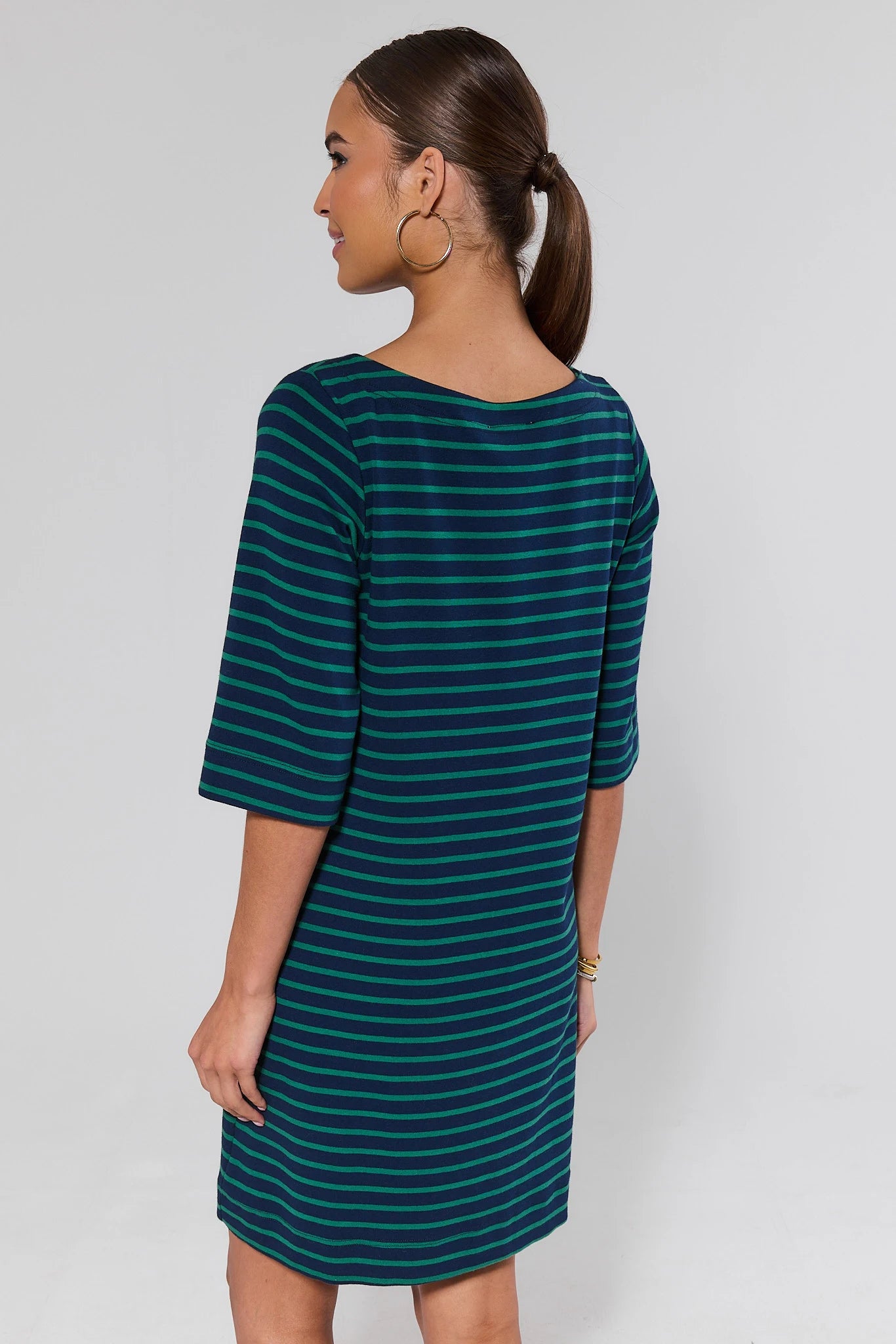 Woman standing wearing a green and blue striped dress against a plain background