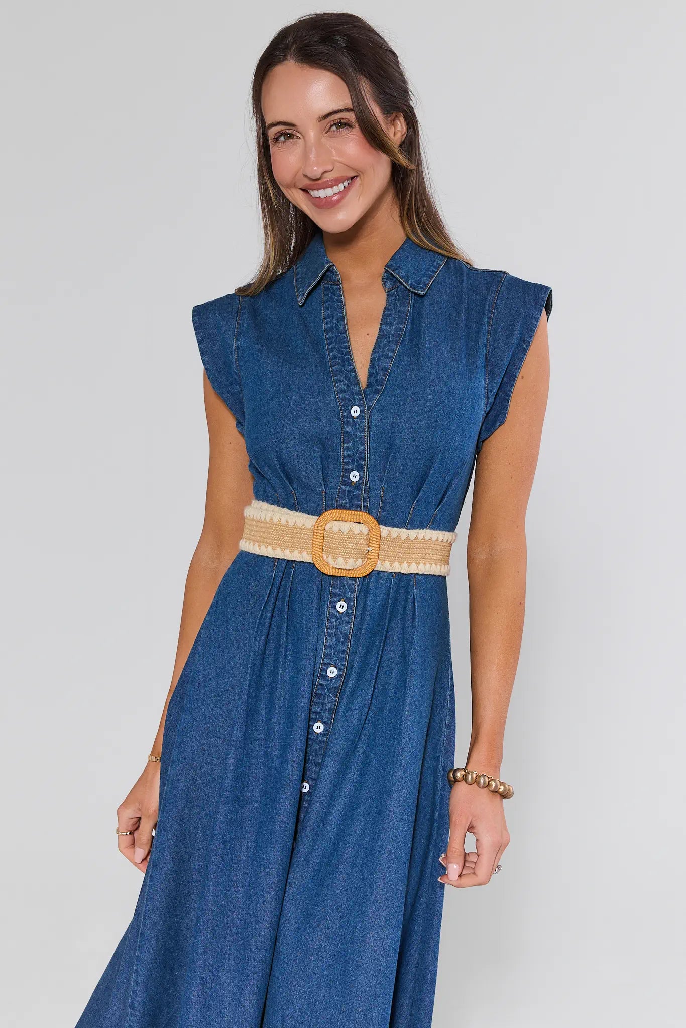 Woman wearing a blue denim dress with a beige belt on a white background
