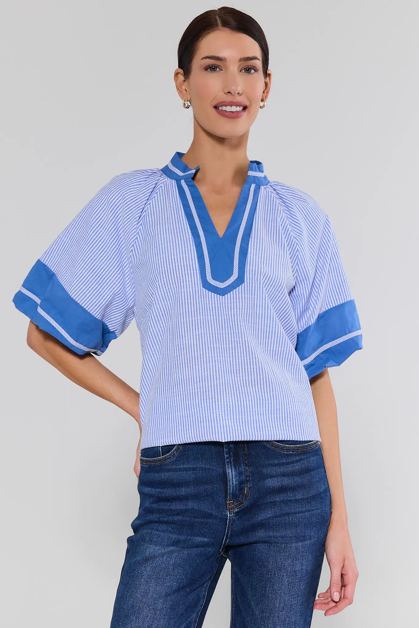 Woman wearing a blue and white striped shirt with rolled-up sleeves on a plain background