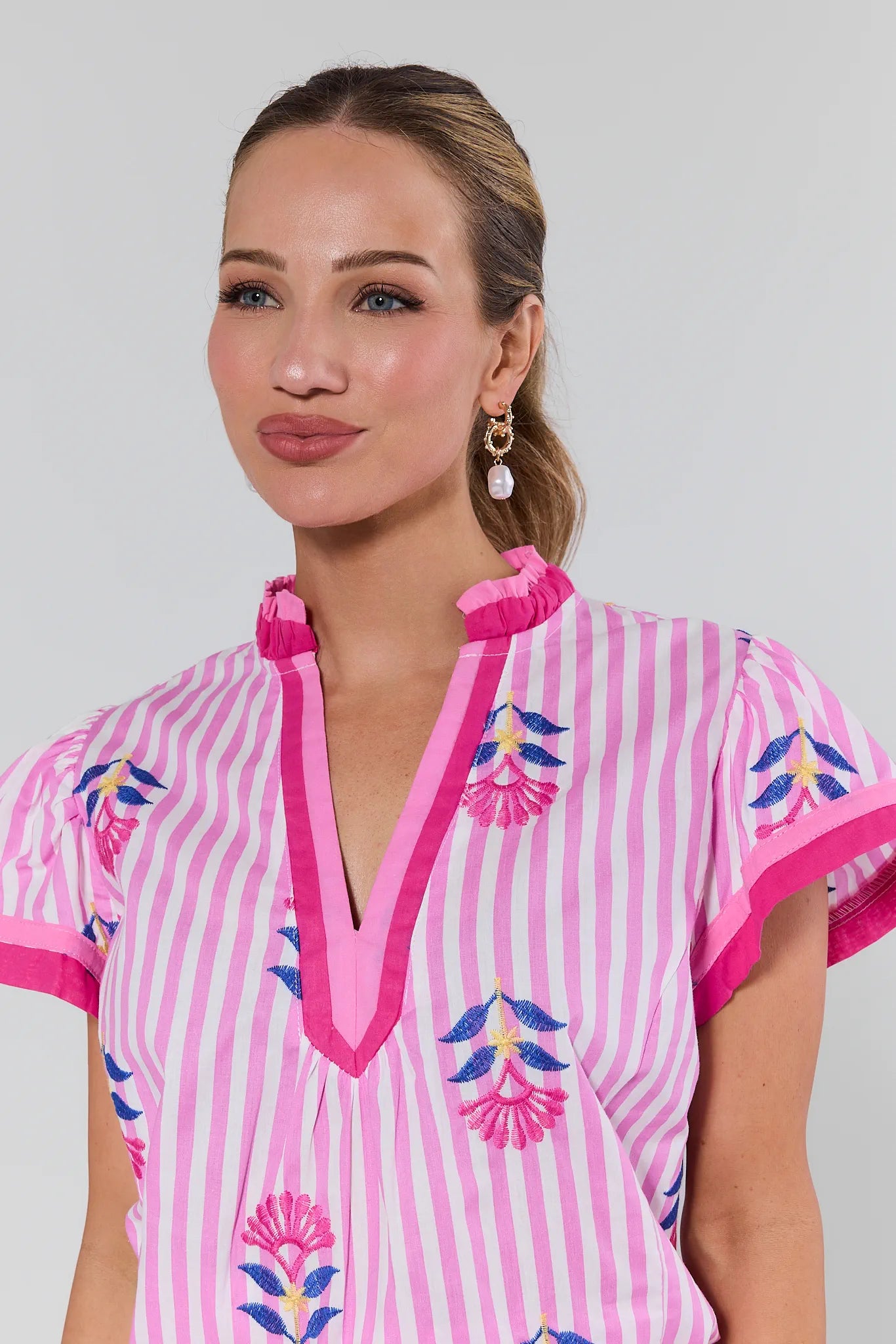 Woman wearing a pink and white striped dress with floral embroidery on a plain background