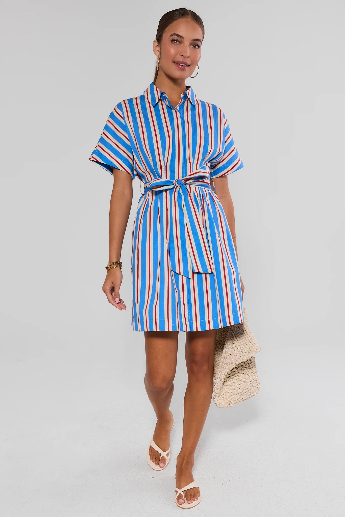 Woman wearing a blue, red, and white striped dress against a plain background standing