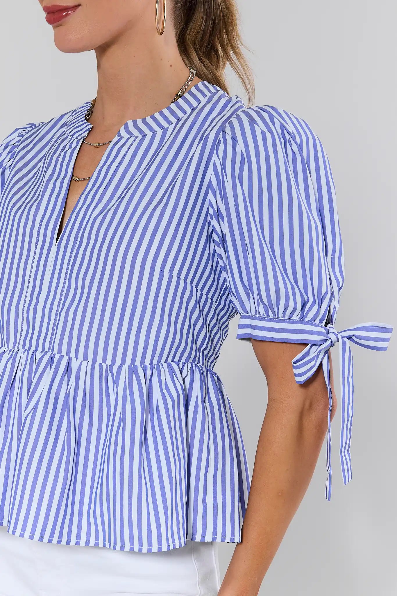 close up Blue and white striped blouse with tied sleeves on a plain background