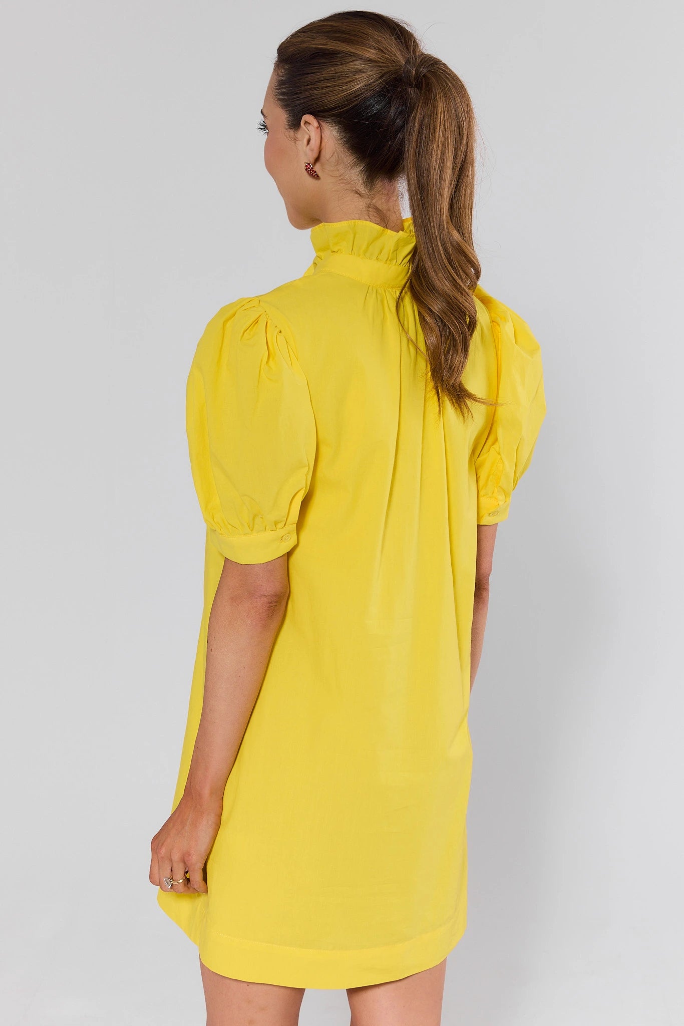 Woman standing wearing a yellow dress with puffed sleeves on a plain background