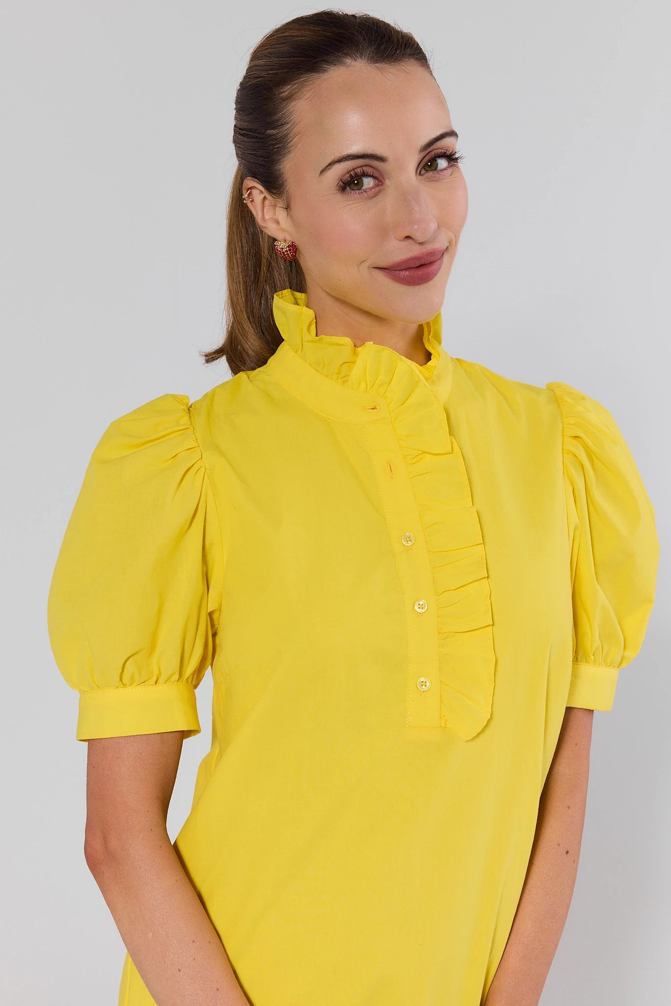 close up Woman wearing a yellow blouse with puff sleeves against a plain background