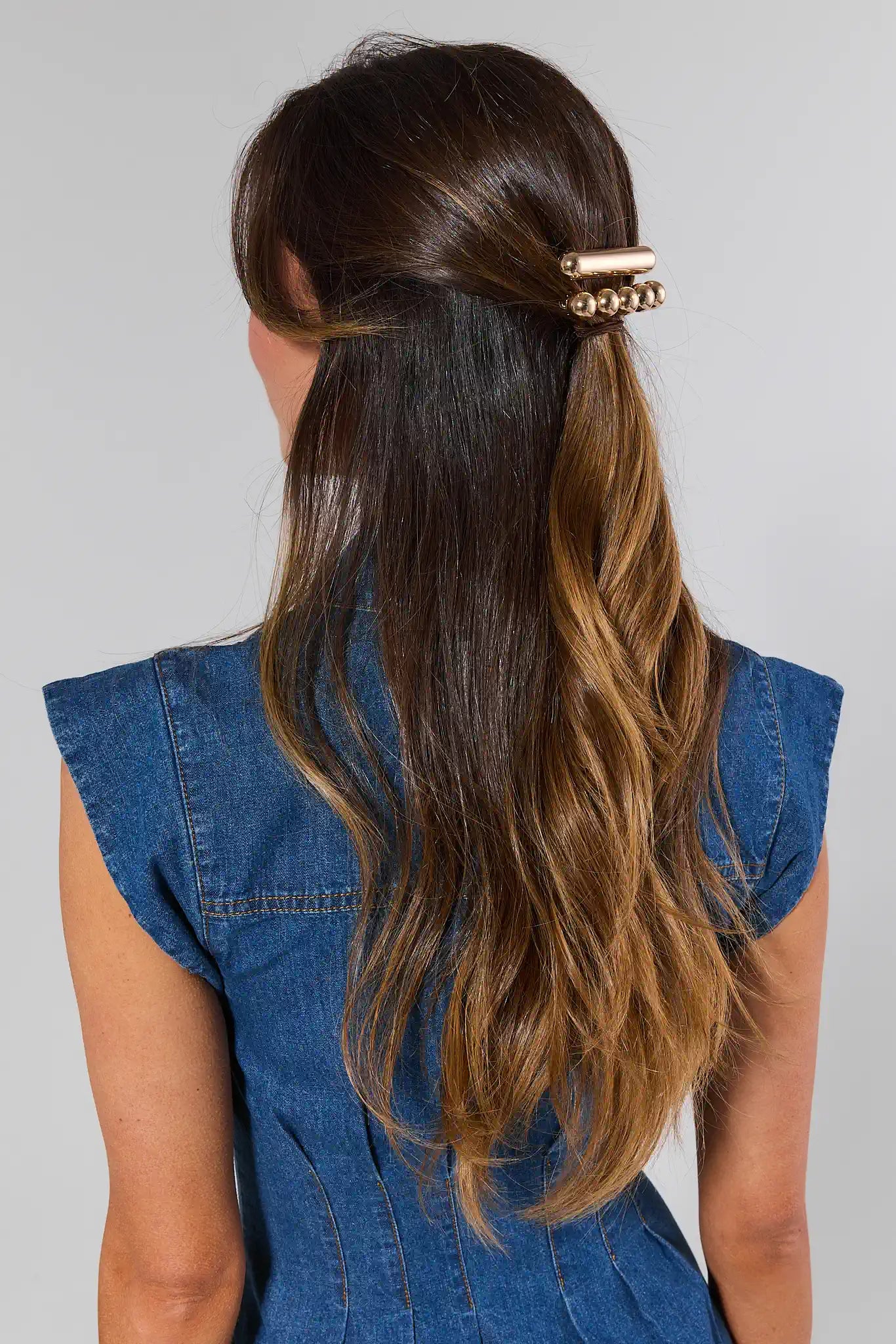 Person with long, wavy hair tied back with a hair clip, wearing a denim dress.