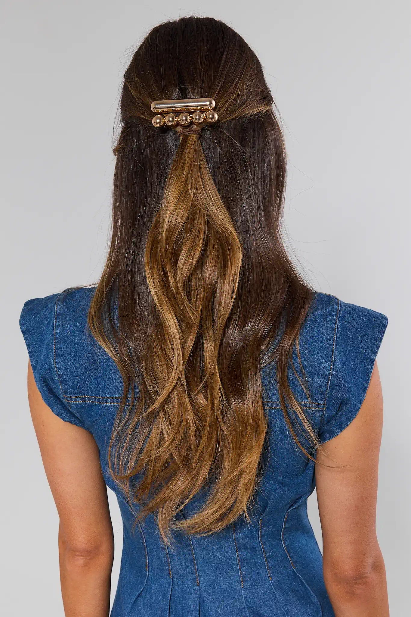 Woman with long, wavy hair wearing a gold hair clip against a plain background