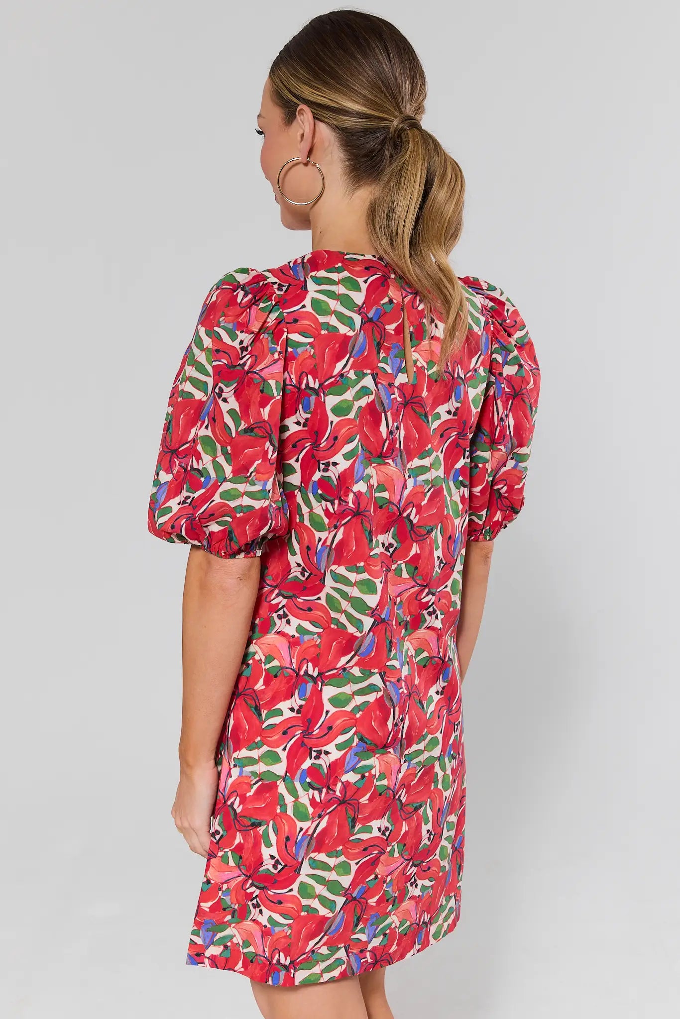 Woman standing wearing a colorful floral dress against a plain background
