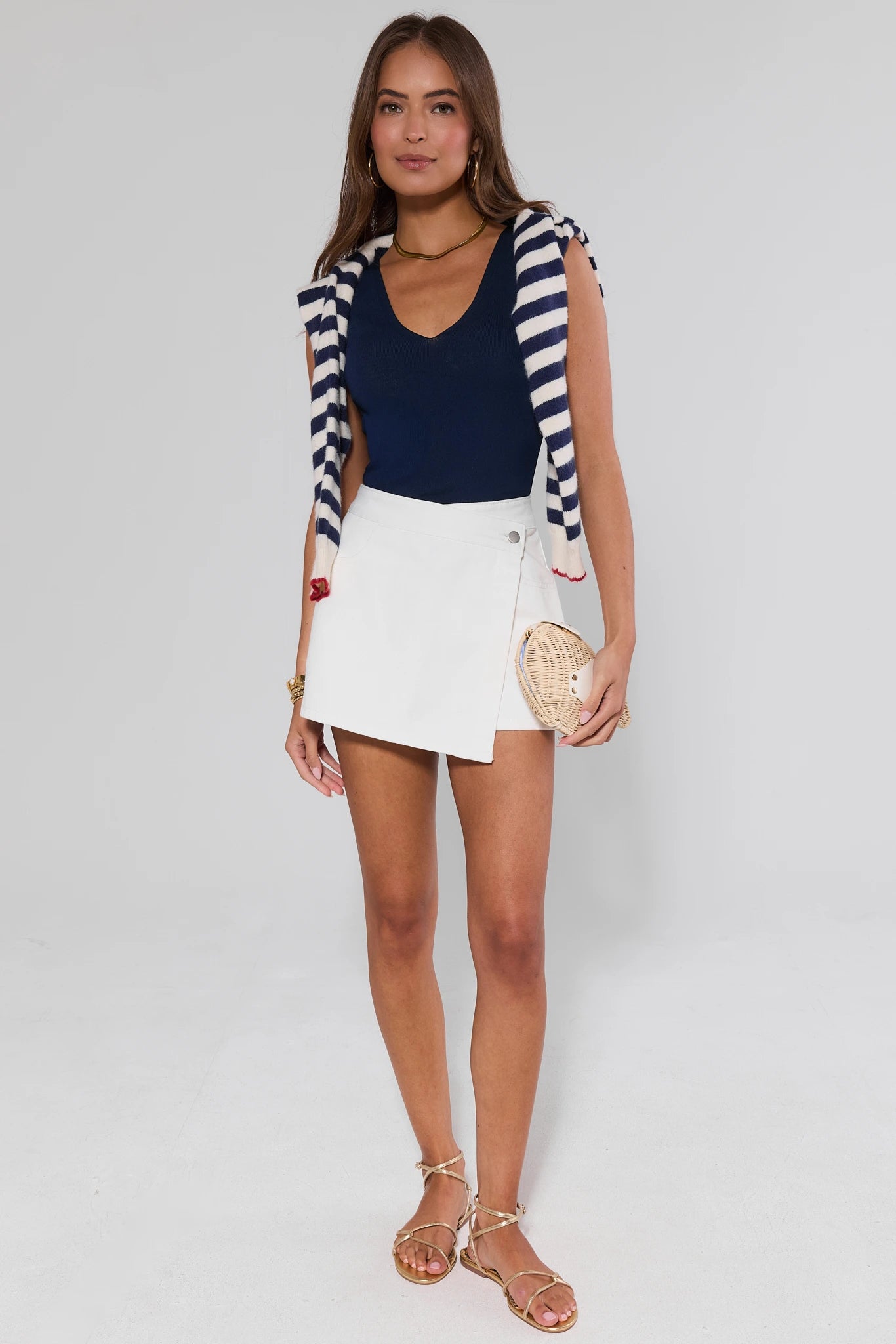 Woman wearing a navy top, white skirt, and striped cardigan on a plain background
