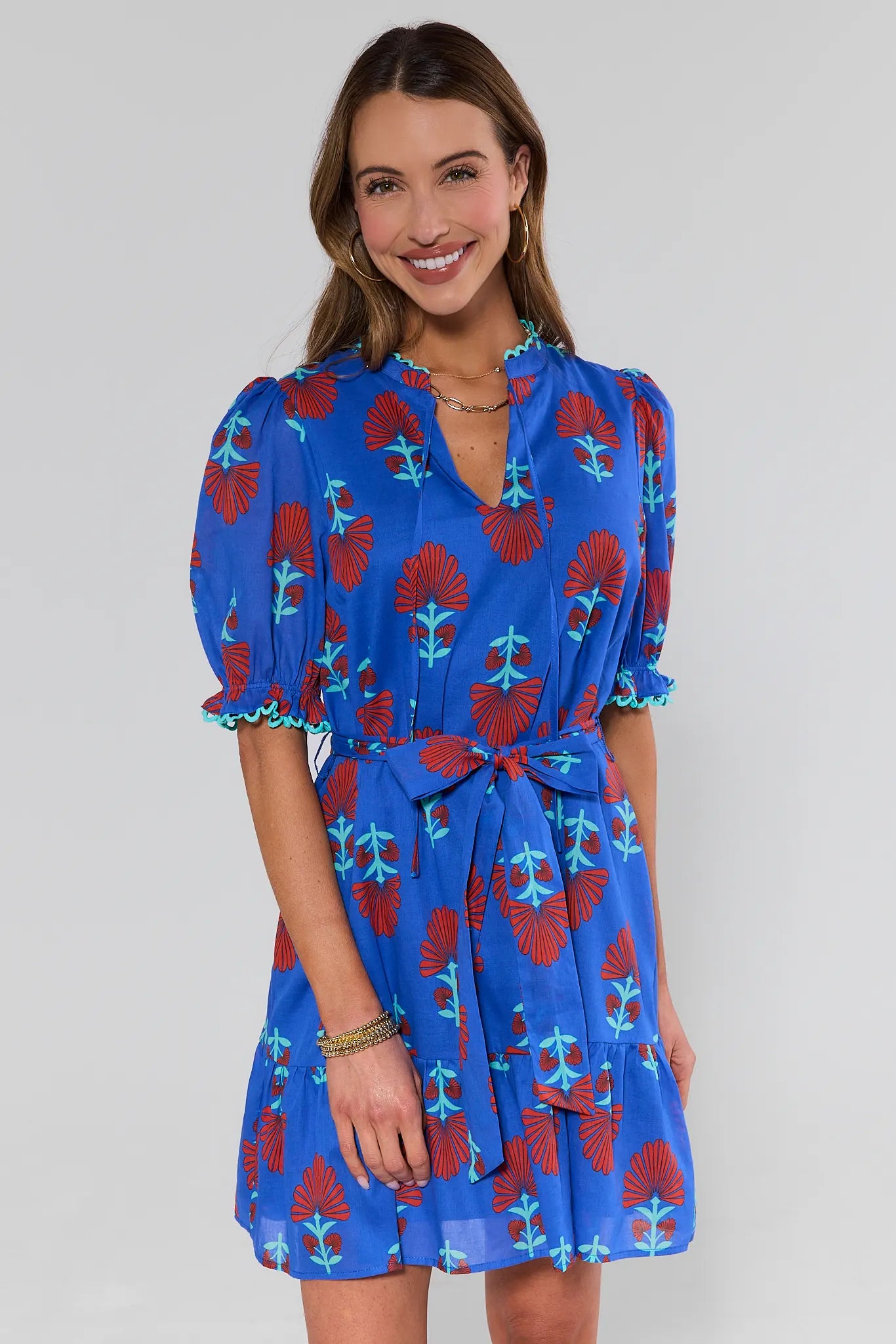 Woman wearing a blue dress with red floral pattern on a plain background