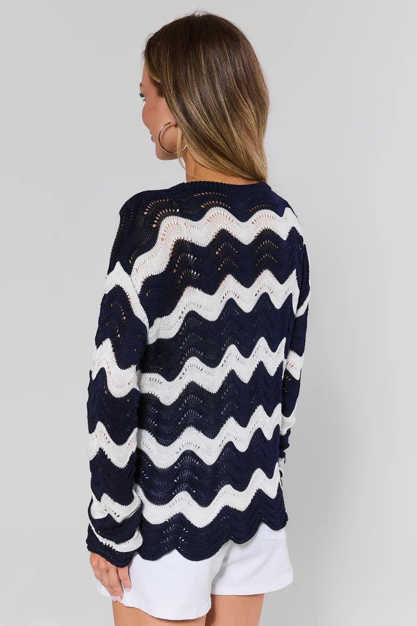 Woman standing wearing a navy and white zigzag patterned sweater on a plain background