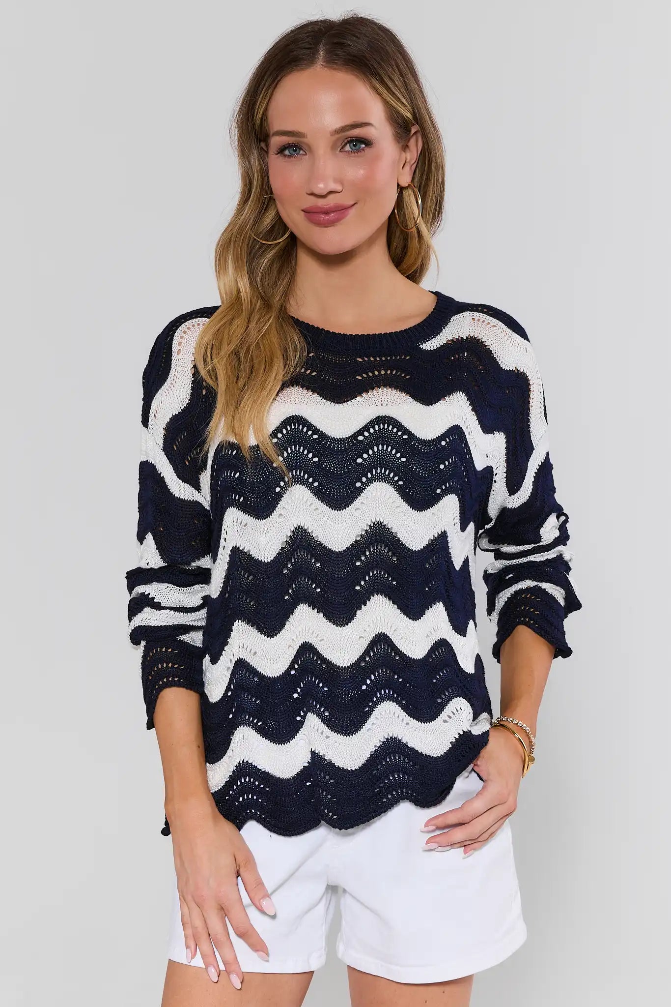 Woman wearing a navy and white striped sweater with white shorts on a plain background