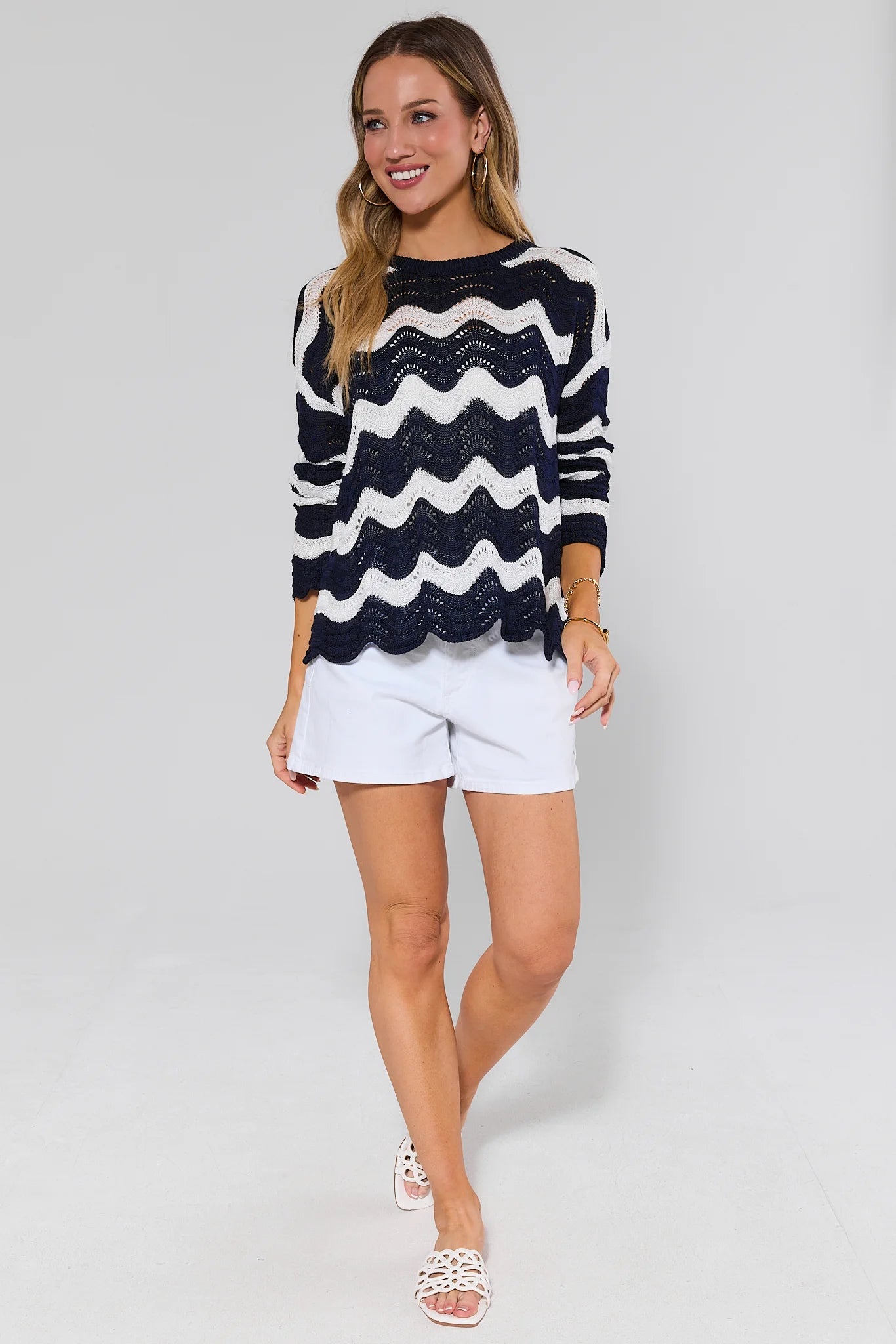 Woman wearing a navy and white striped sweater with white shorts on a plain background