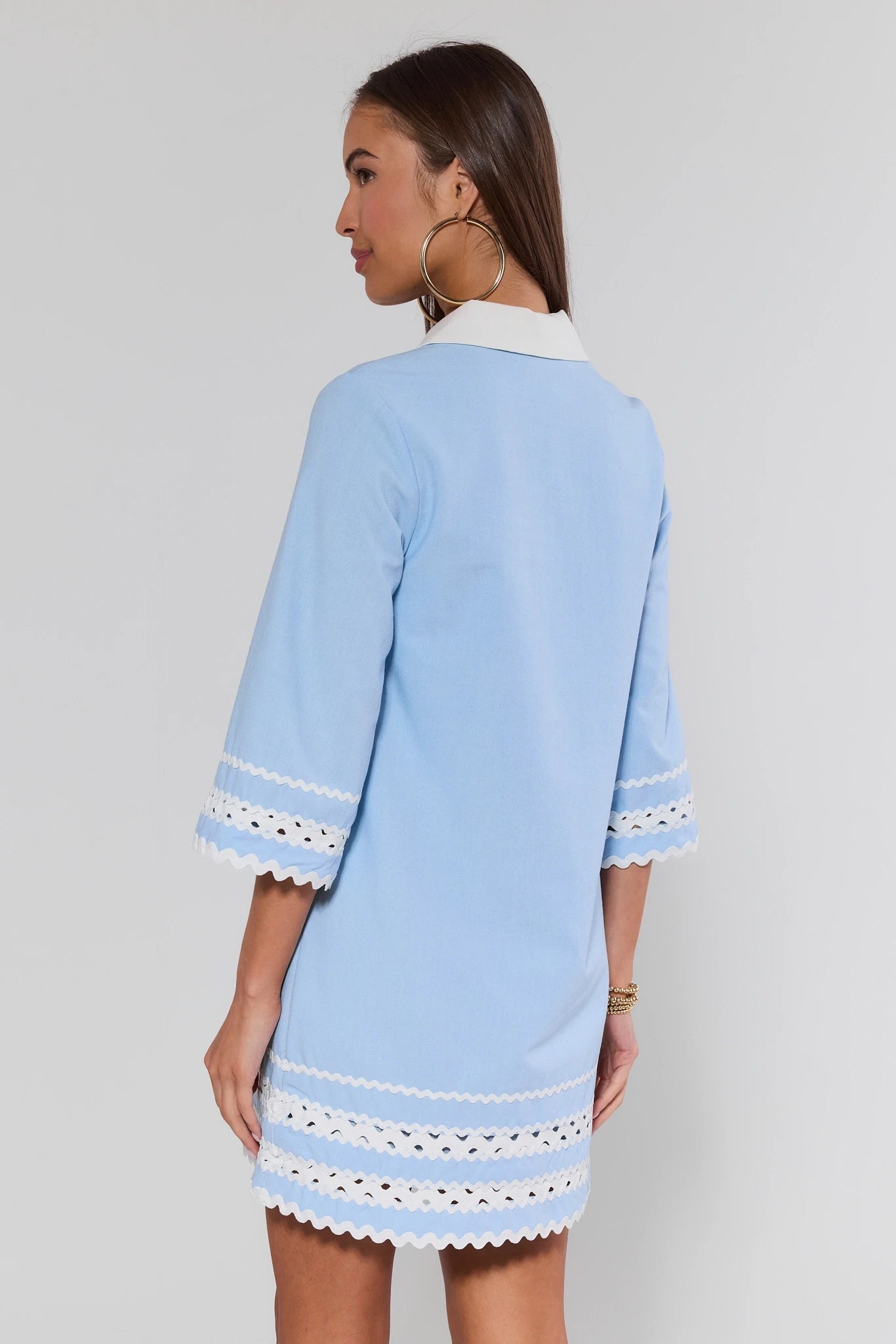 Woman wearing a light blue dress with white lace trim on a plain background