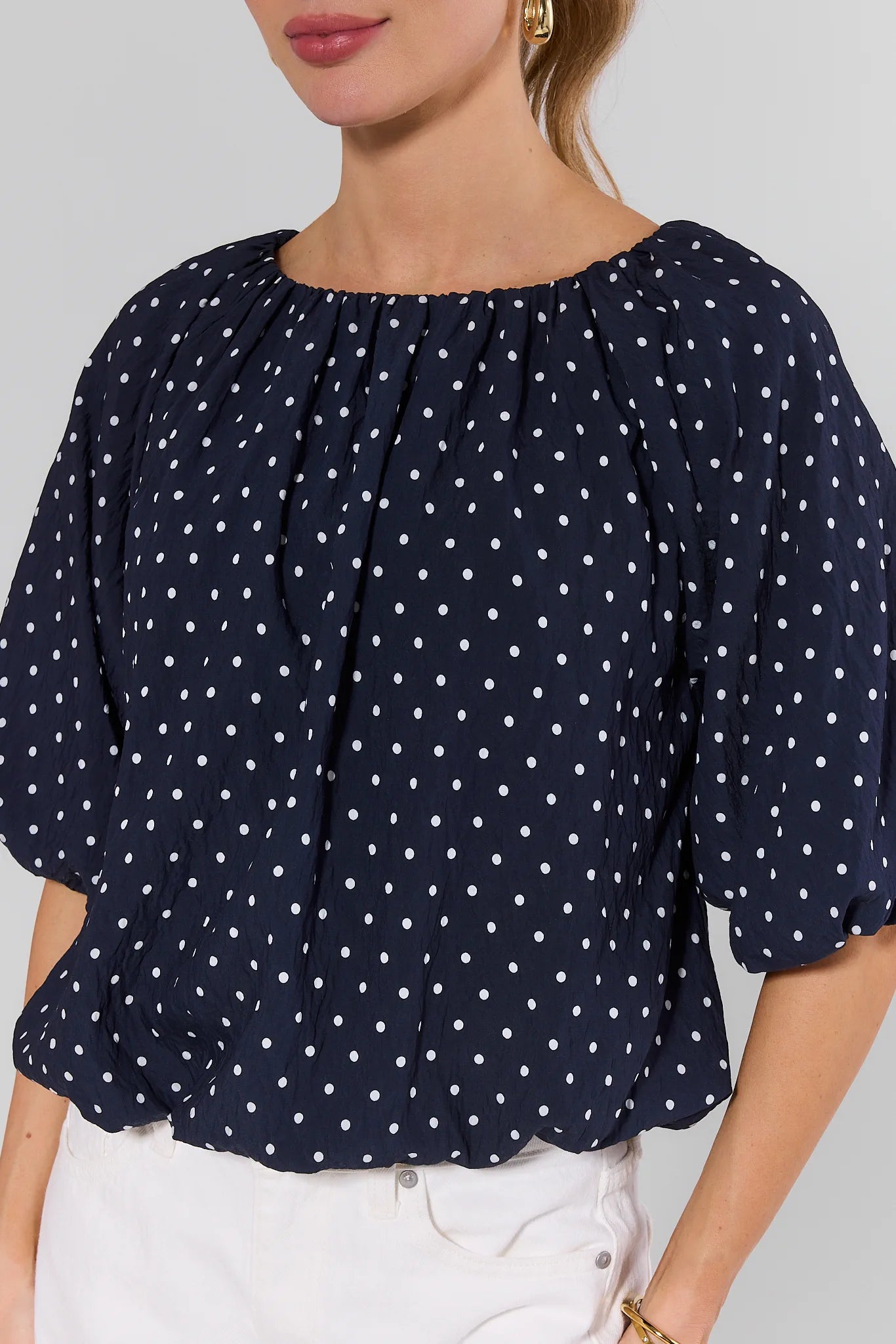 Navy blue blouse with white polka dots worn by a person on a light gray background