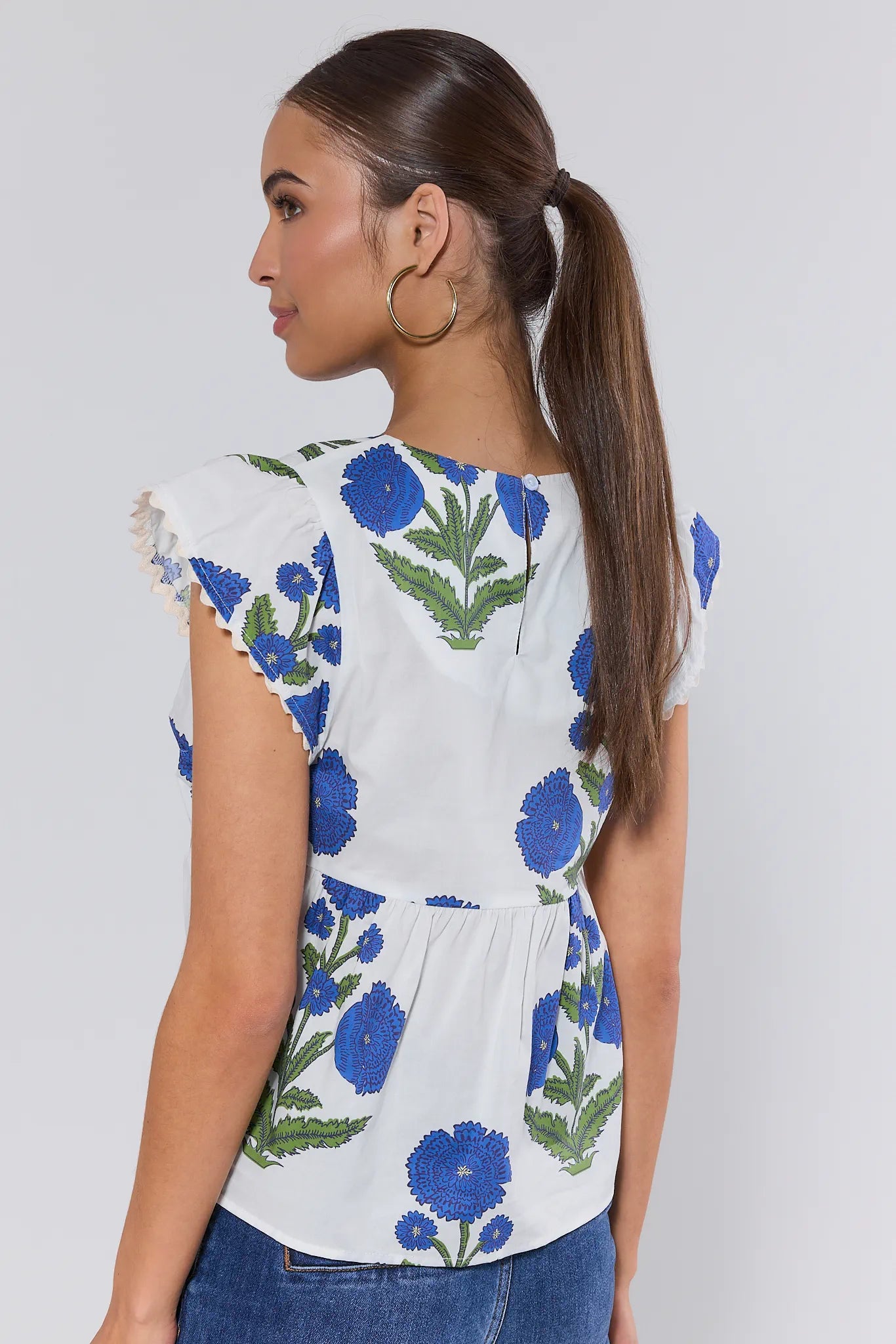 Woman wearing a white top with blue floral patterns on a plain background