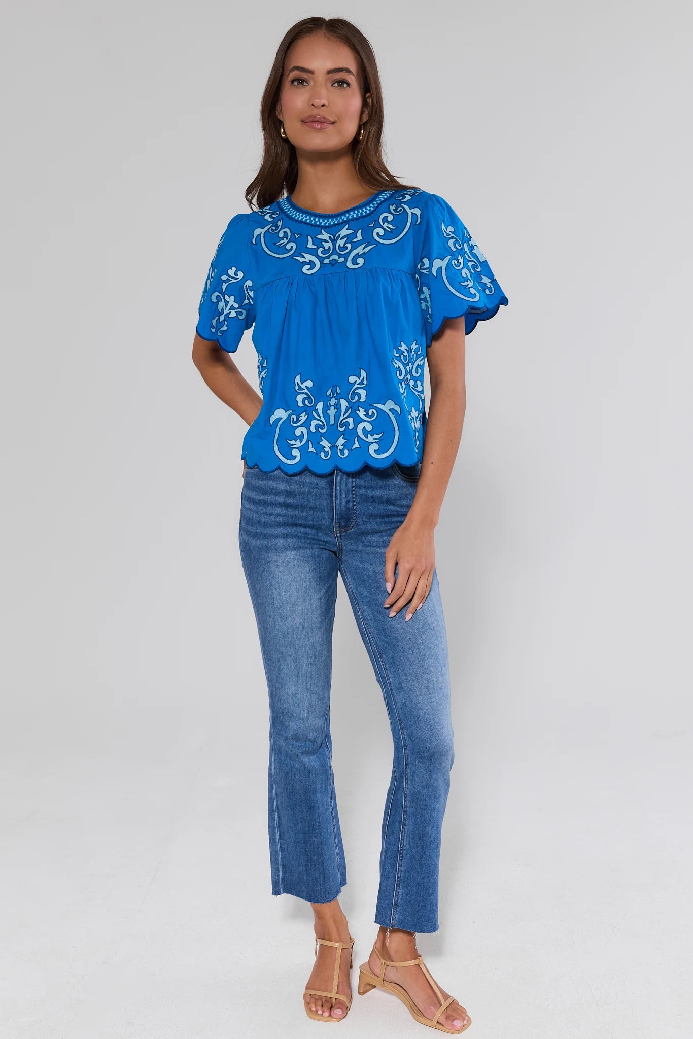 Woman wearing a blue embroidered top and jeans on a white background