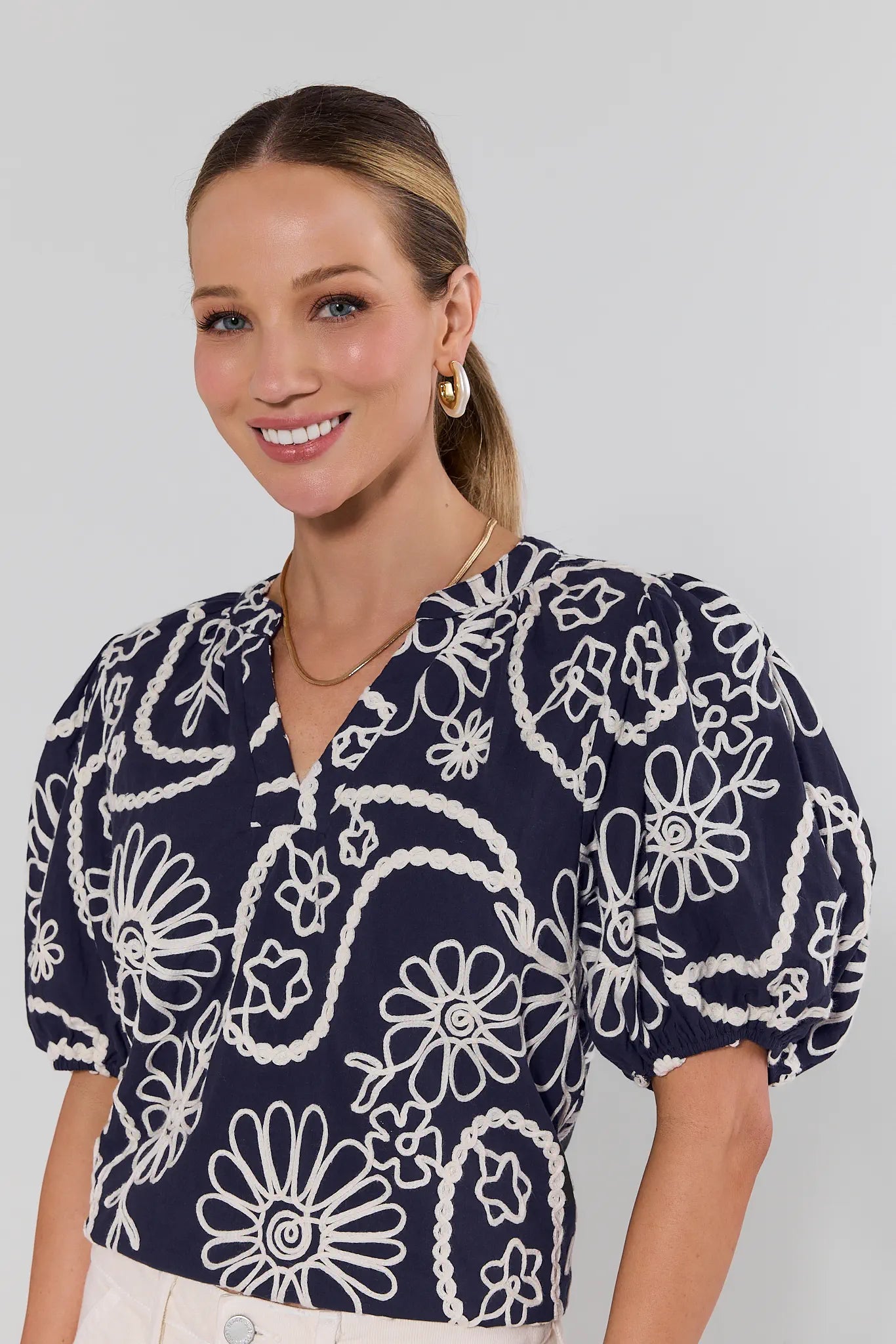 Woman wearing a navy blue blouse with white floral patterns on a plain background