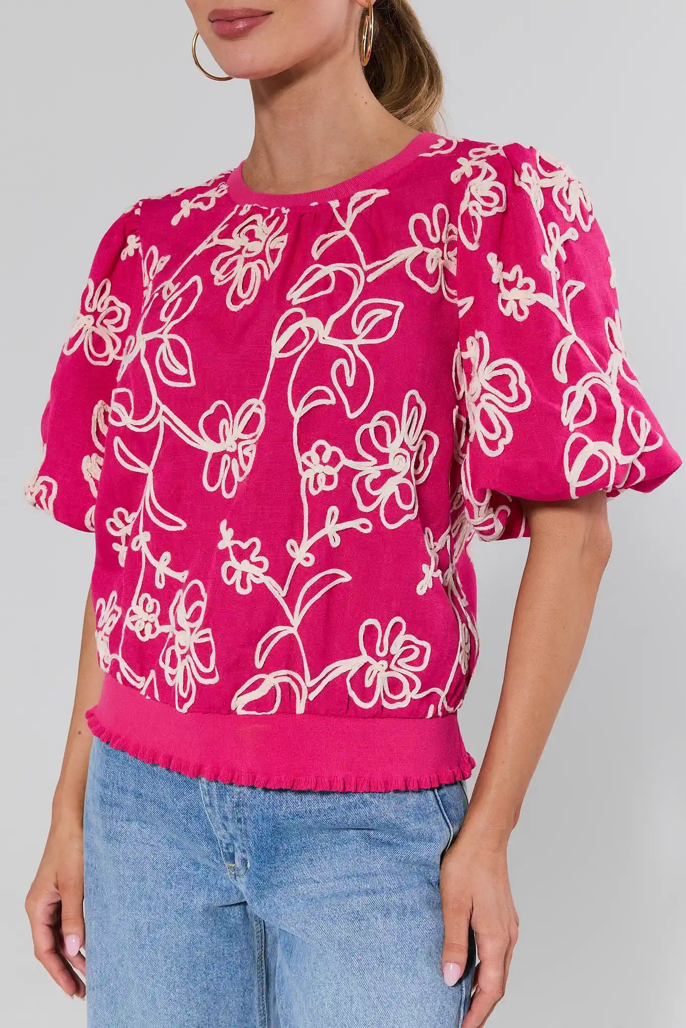 Woman wearing a pink floral blouse with blue jeans on a plain background