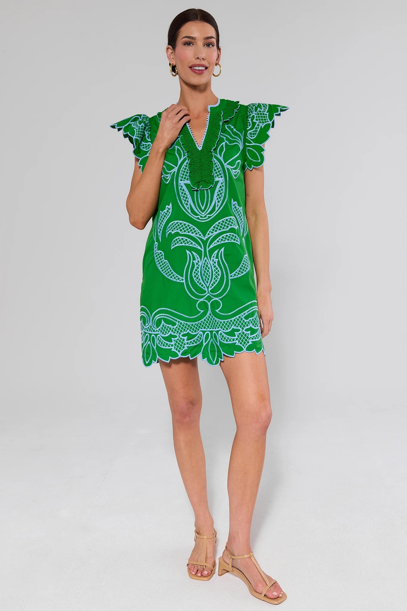 Woman wearing a green embroidered dress with blue patterns on a gray background