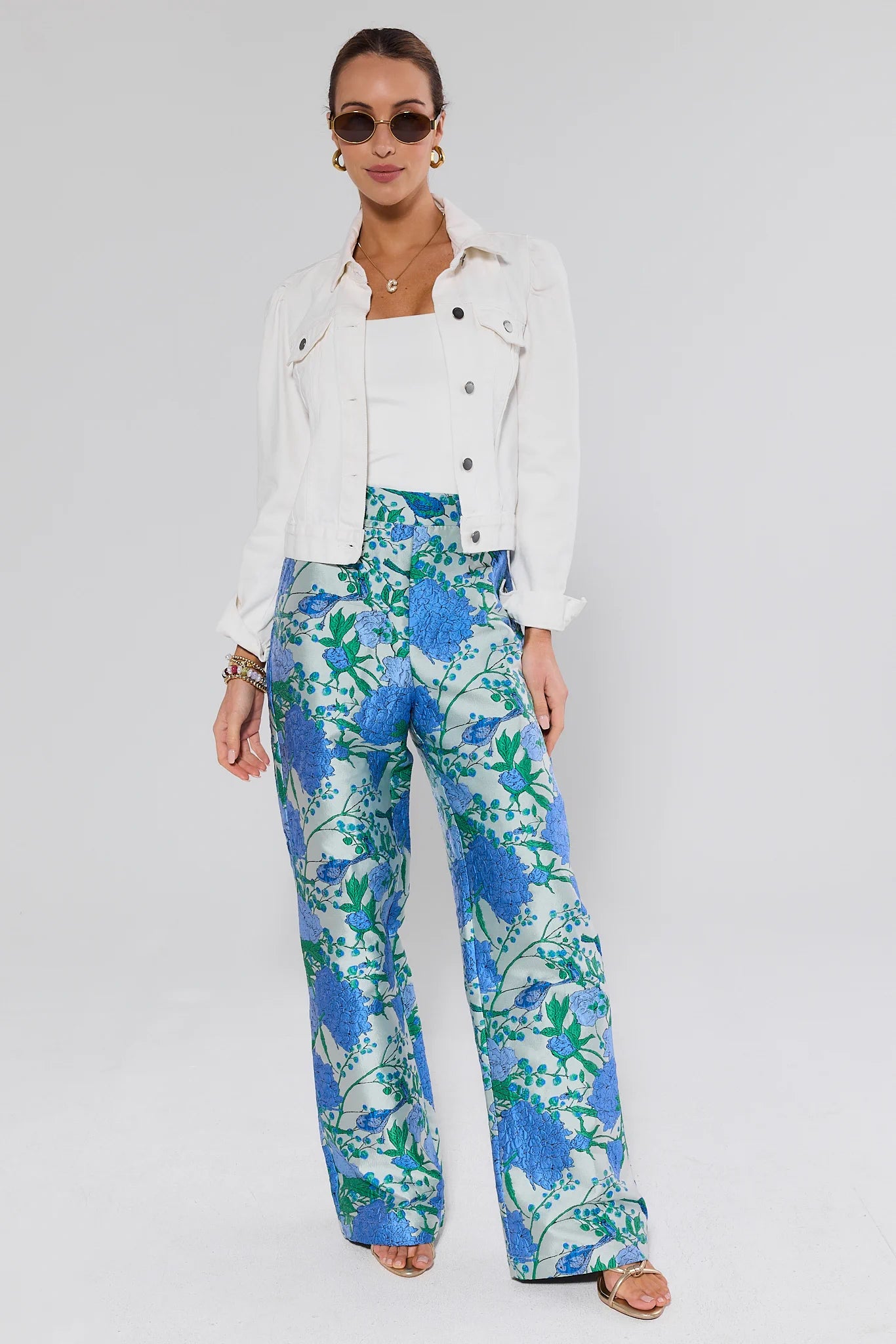 Woman wearing a white jacket and blue floral pants on a gray background