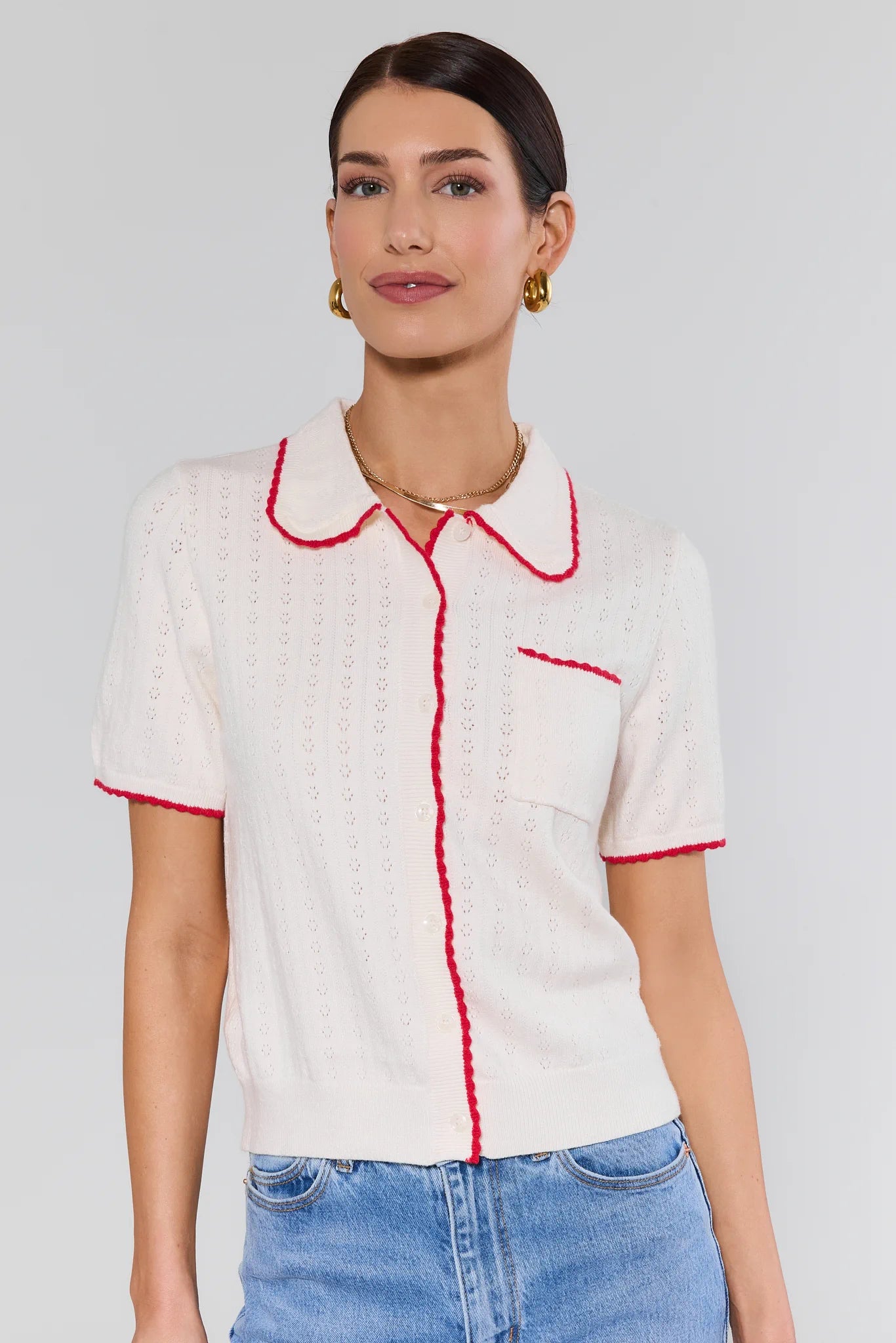 Woman wearing a white blouse with red trim and blue jeans on a plain background