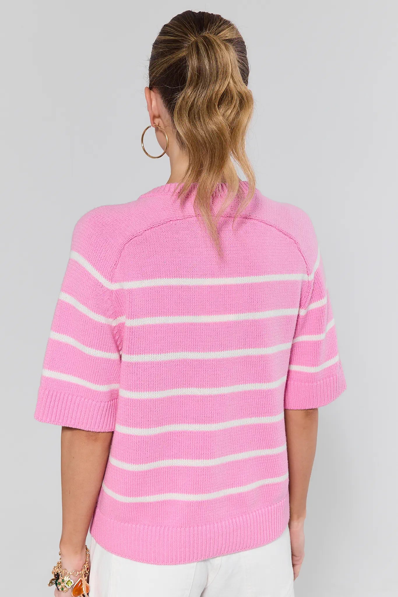 Person standing wearing a pink and white striped sweater on a plain background