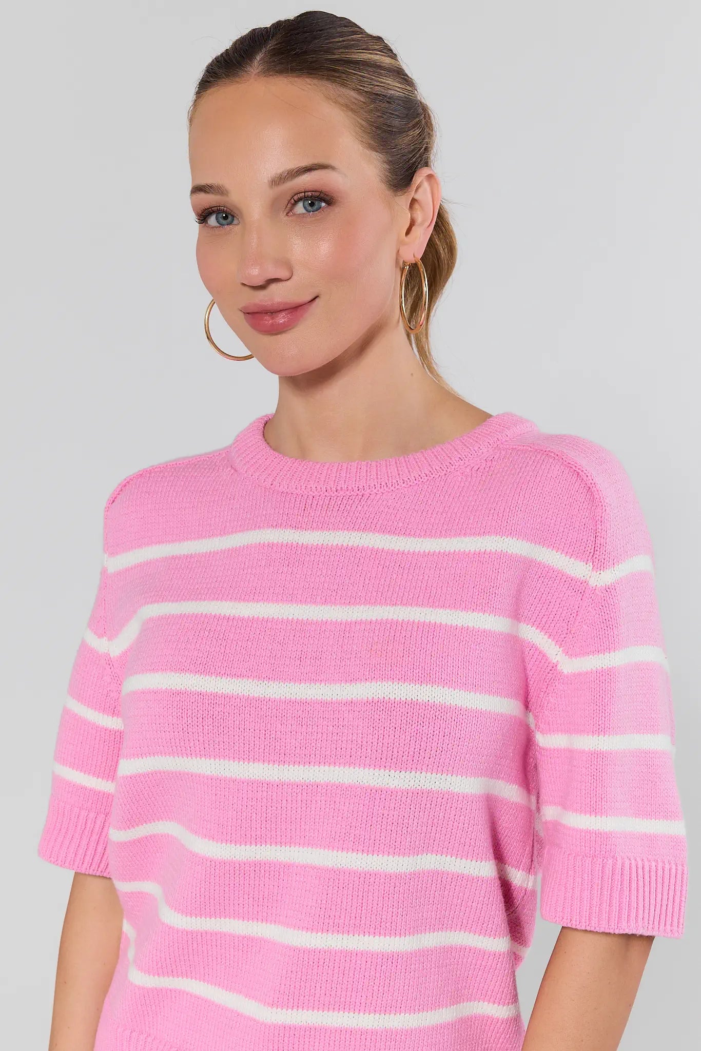 Woman wearing a pink striped sweater against a plain background