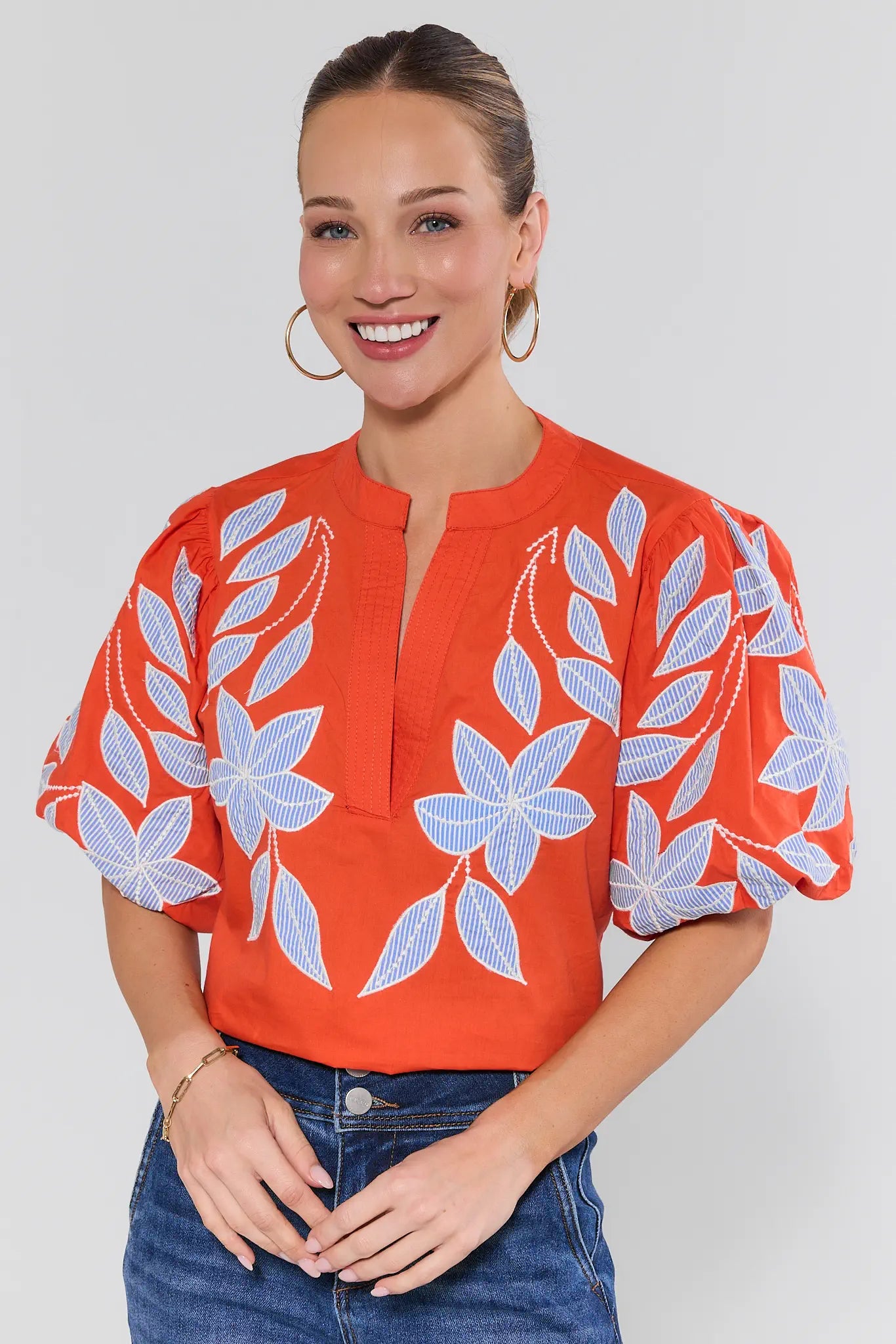 Woman wearing an orange blouse with white floral patterns on a plain background