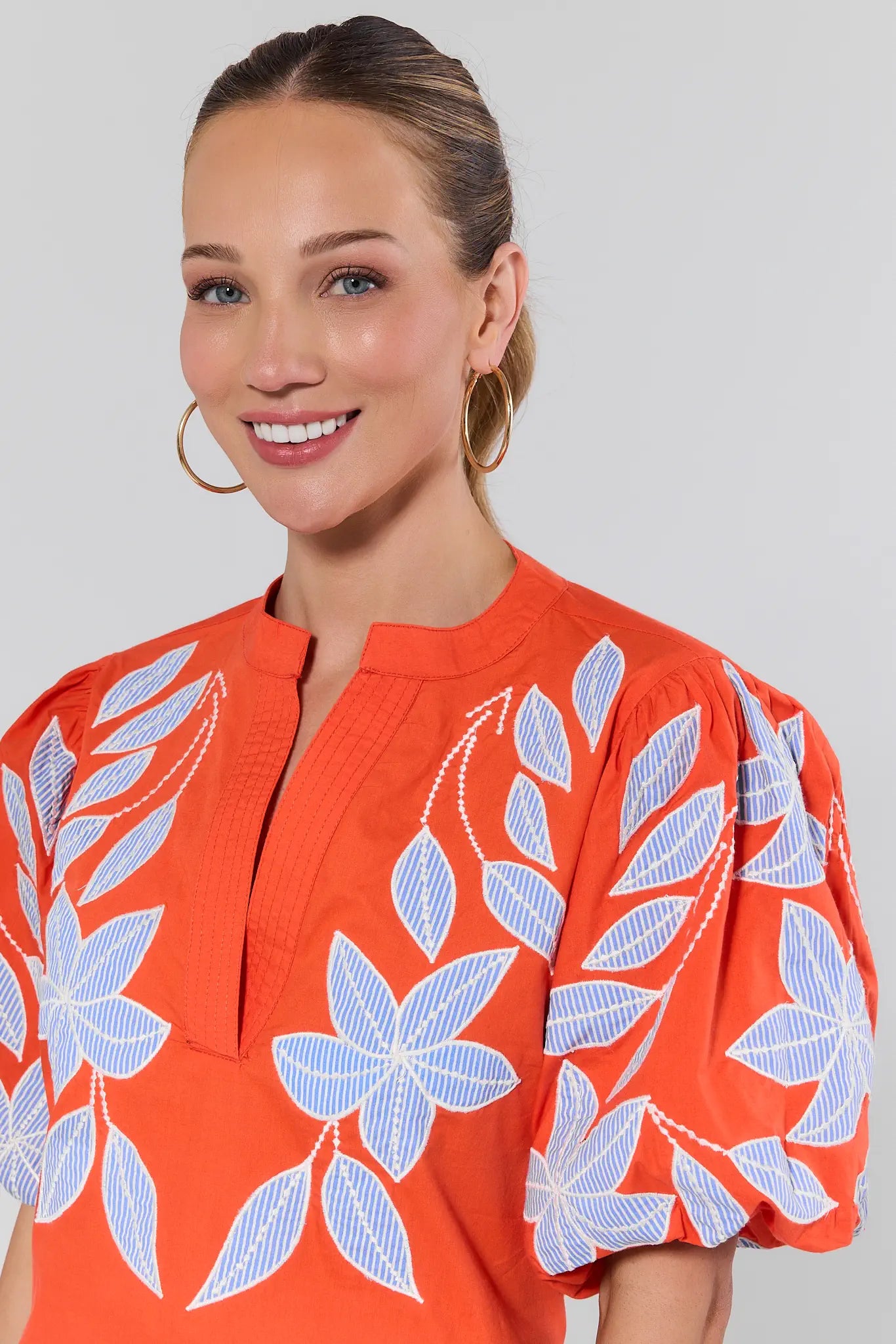 Woman wearing an orange blouse with white floral patterns on a plain background
