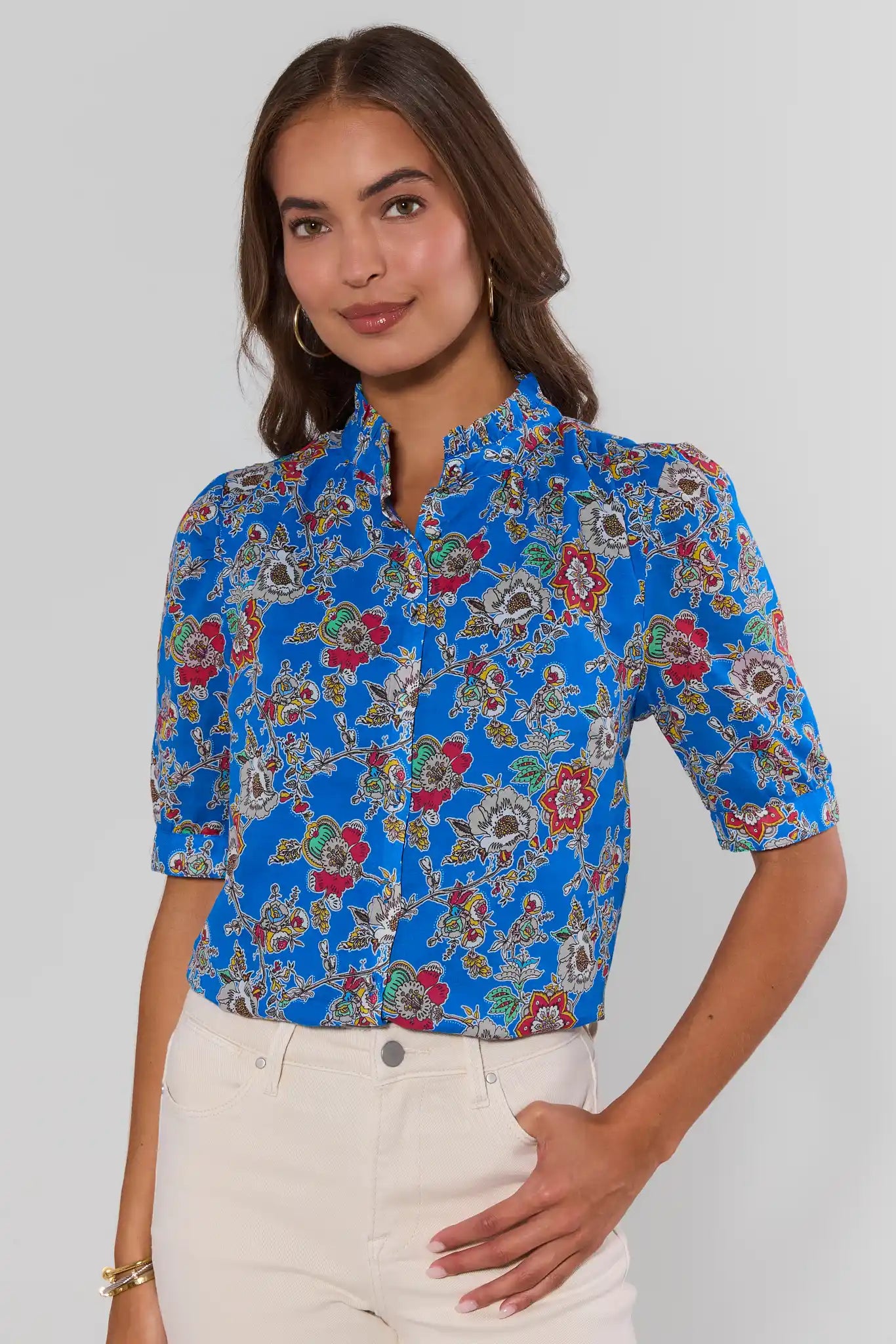 Woman wearing a blue floral blouse against a plain background stand