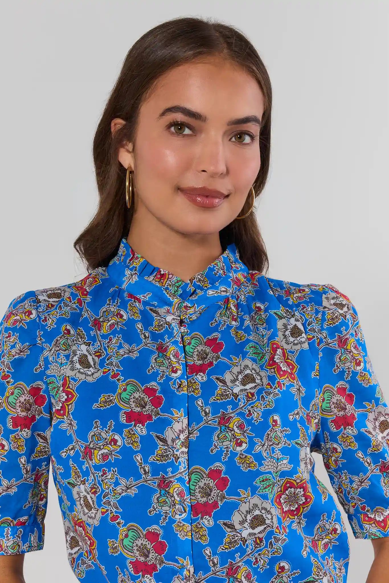 Woman wearing a blue floral patterned blouse against a plain background close up