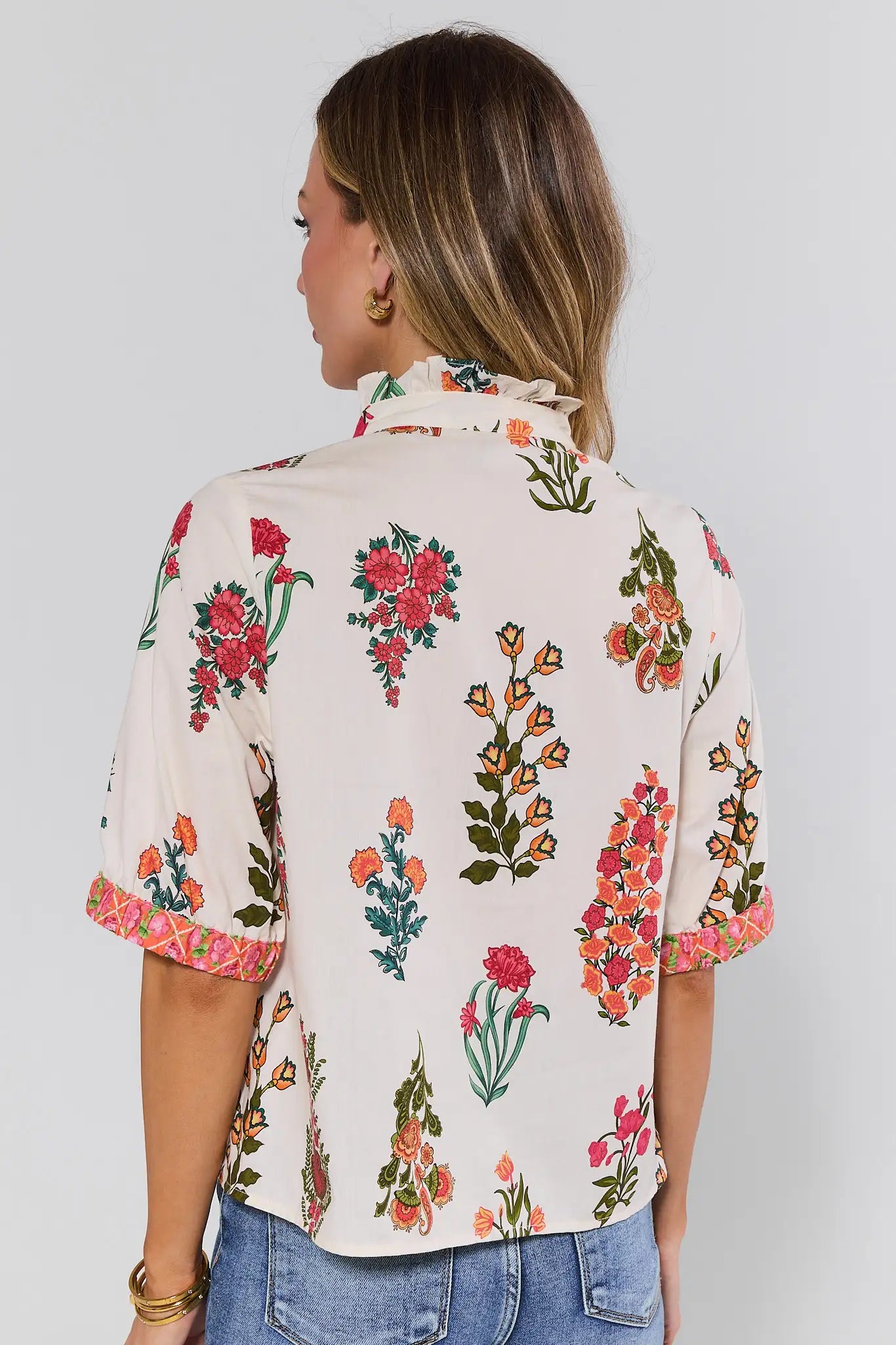 Woman standing wearing a floral blouse with a plain background